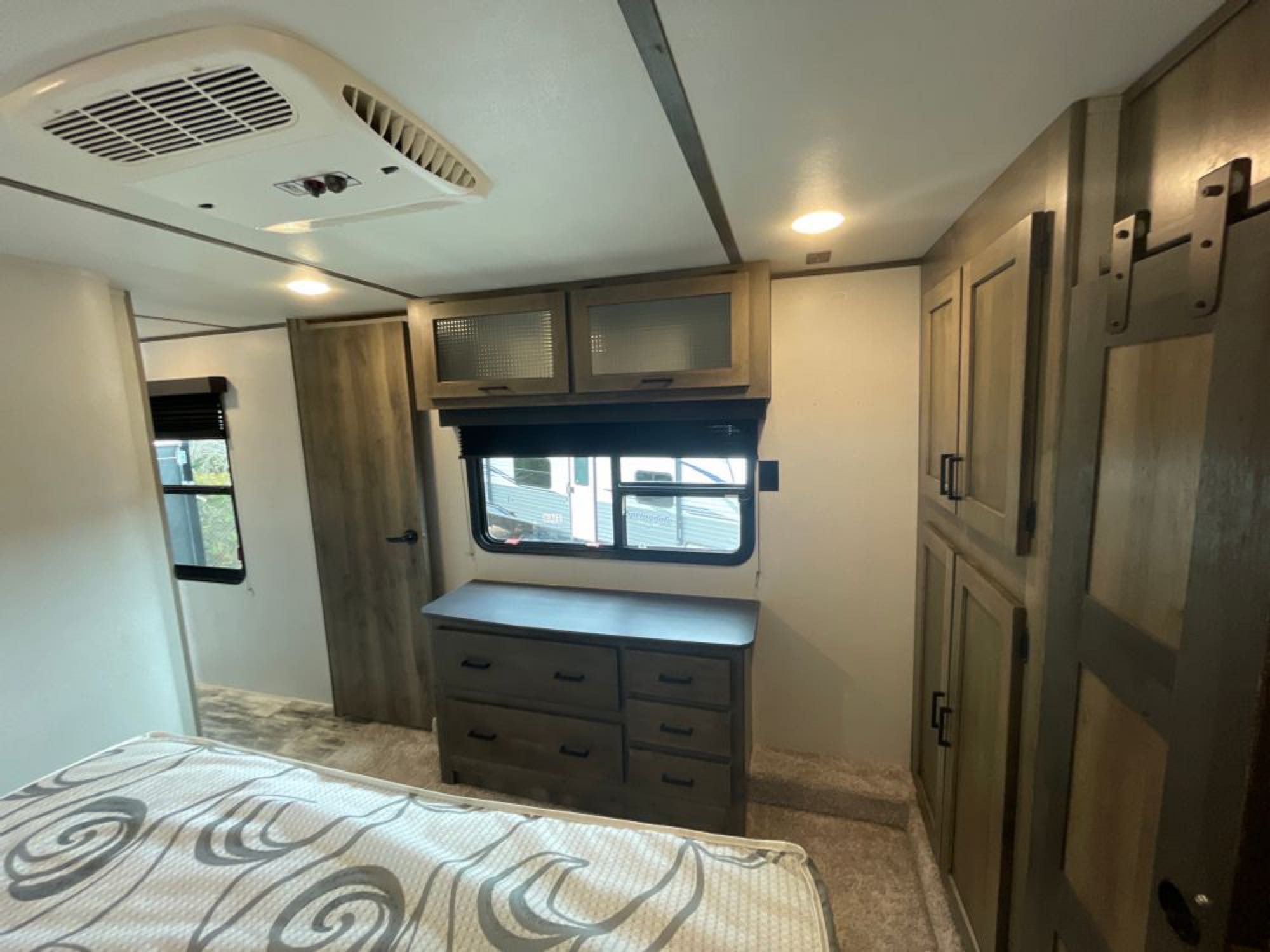 Spacious RV rental bedroom featuring a bed, AC, dresser, and built-in wood cabinets for ample storage.. Keystone RV Sprinter Limited 2021