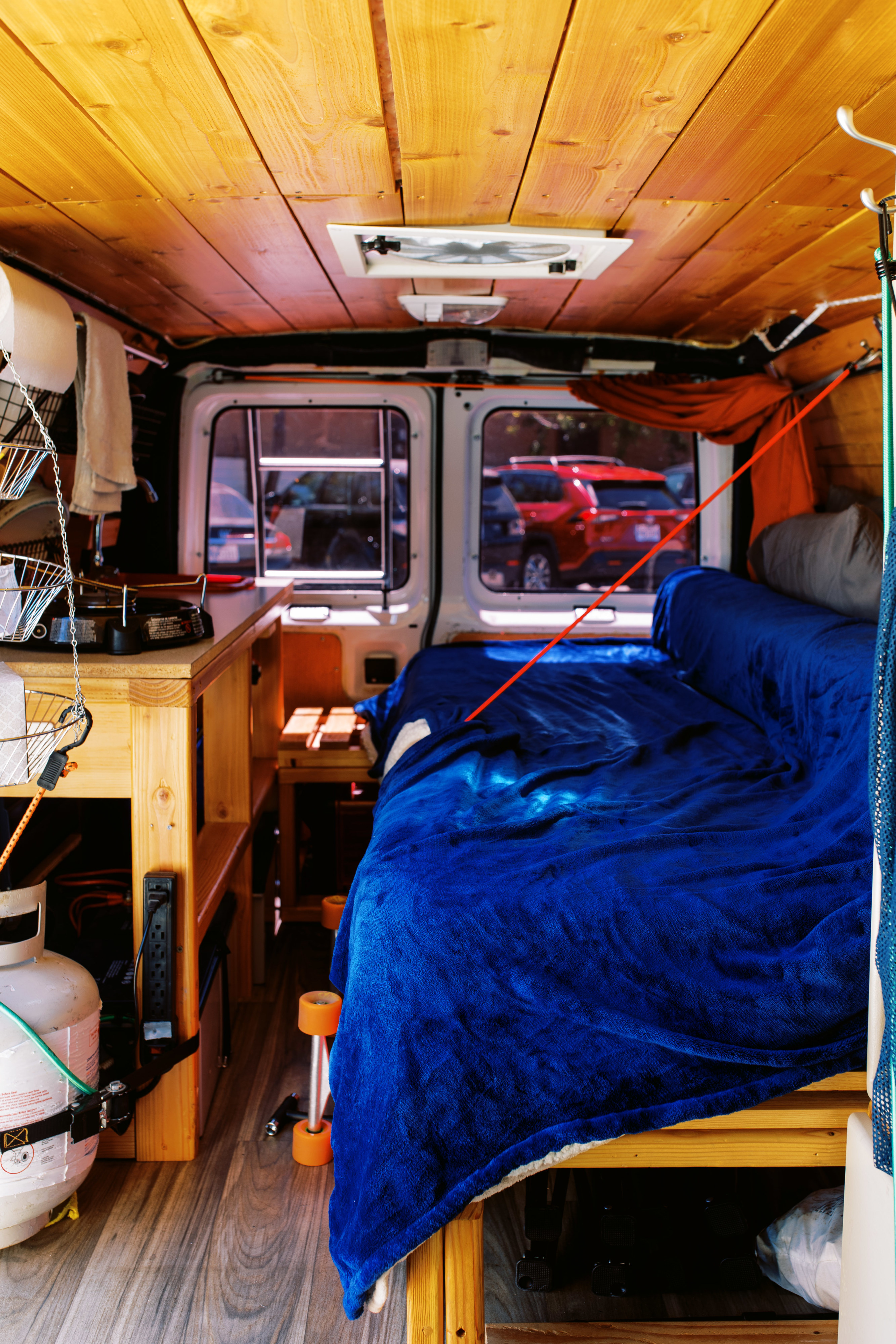 Cozy RV rental interior with a wooden ceiling, blue blanket bed, and kitchen setup, ideal for comfortable van life adventures.. Ford Econoline E250supercab 2007