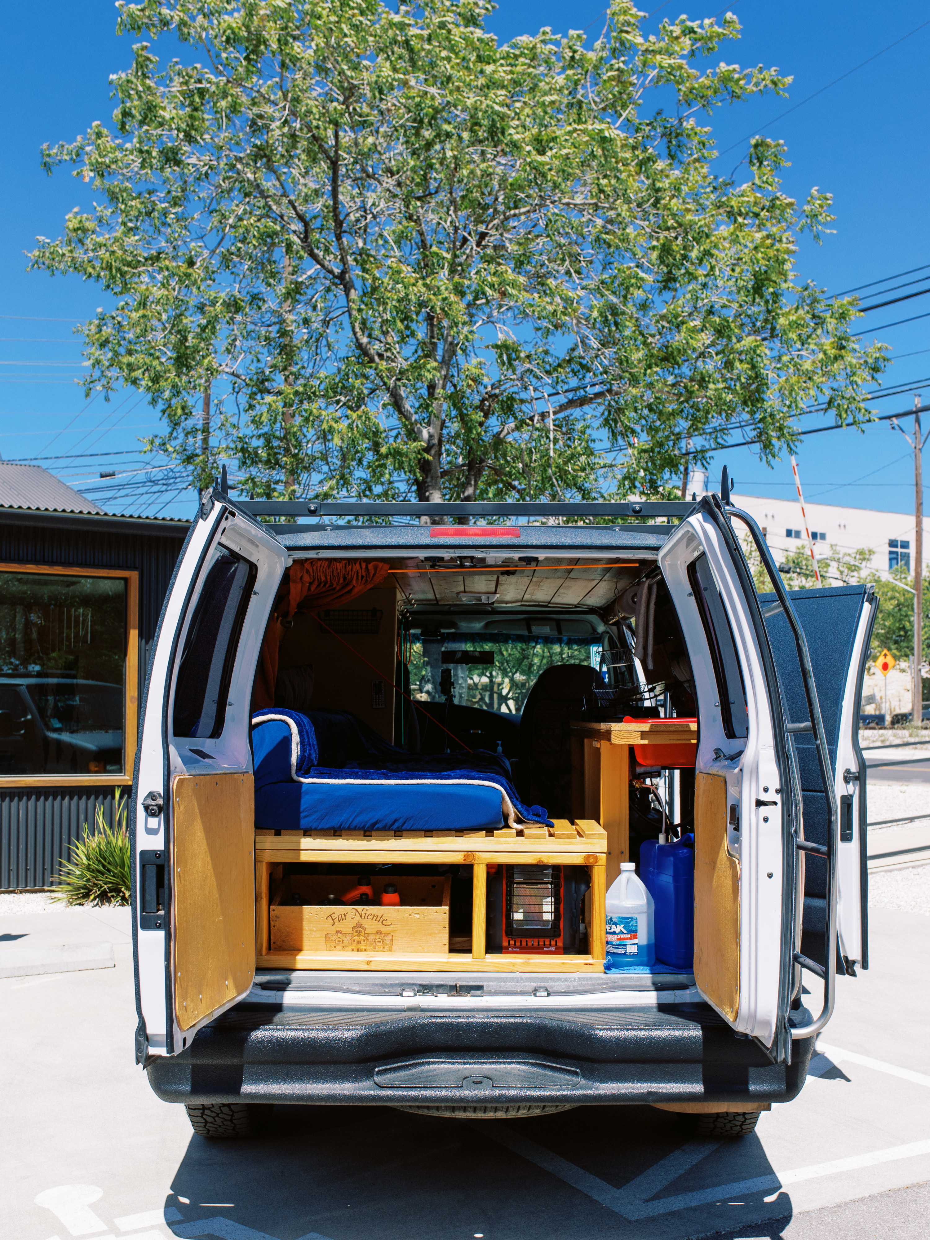 White RV rental with rear doors open, revealing a blue-covered bed, wooden storage, and equipment inside, parked outside.. Ford Econoline E250supercab 2007