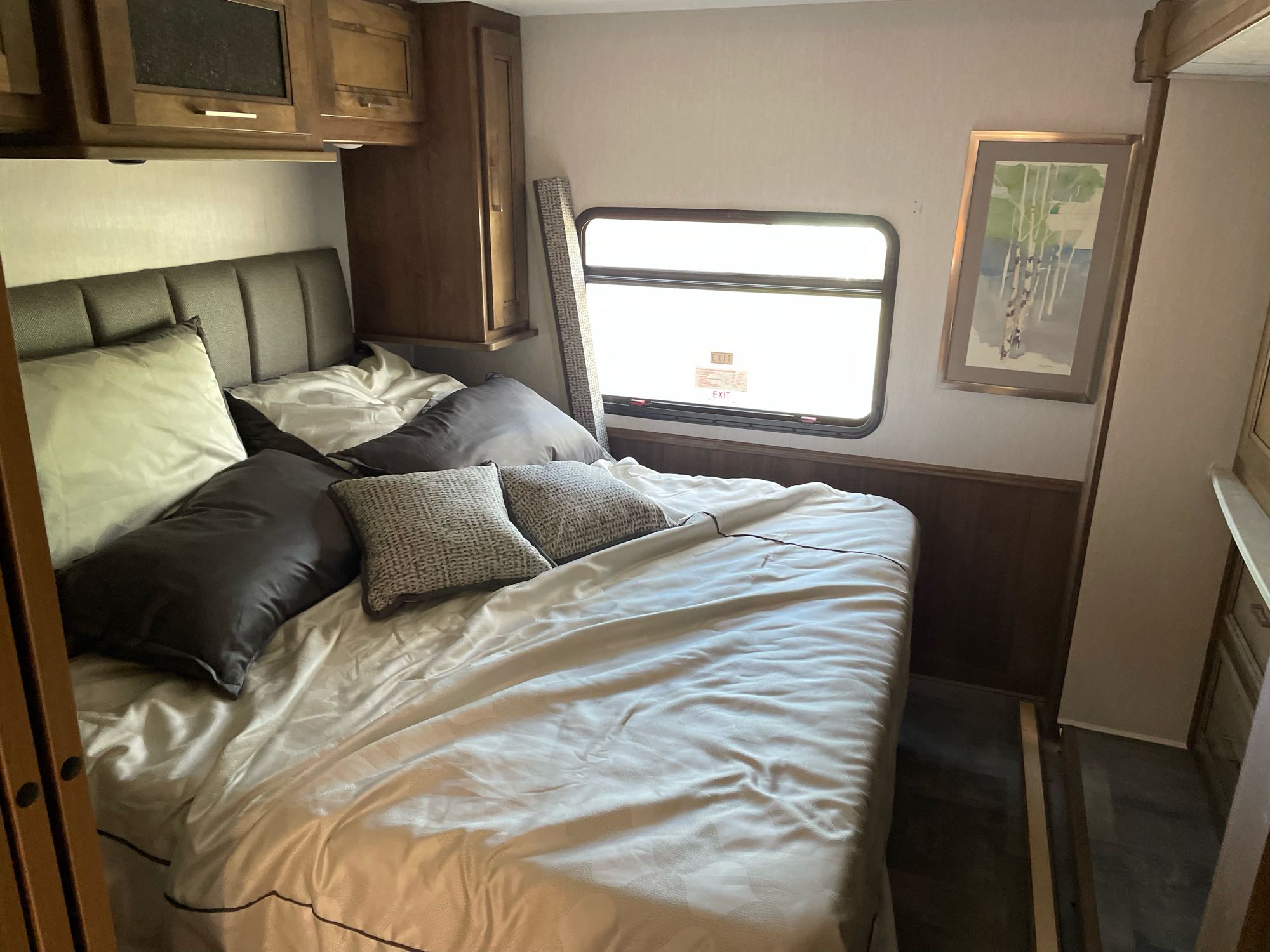 Cozy RV rental bedroom featuring a bed with pillows, wood cabinets, and an emergency exit window.. Coachmen Mirada 32ss 2021