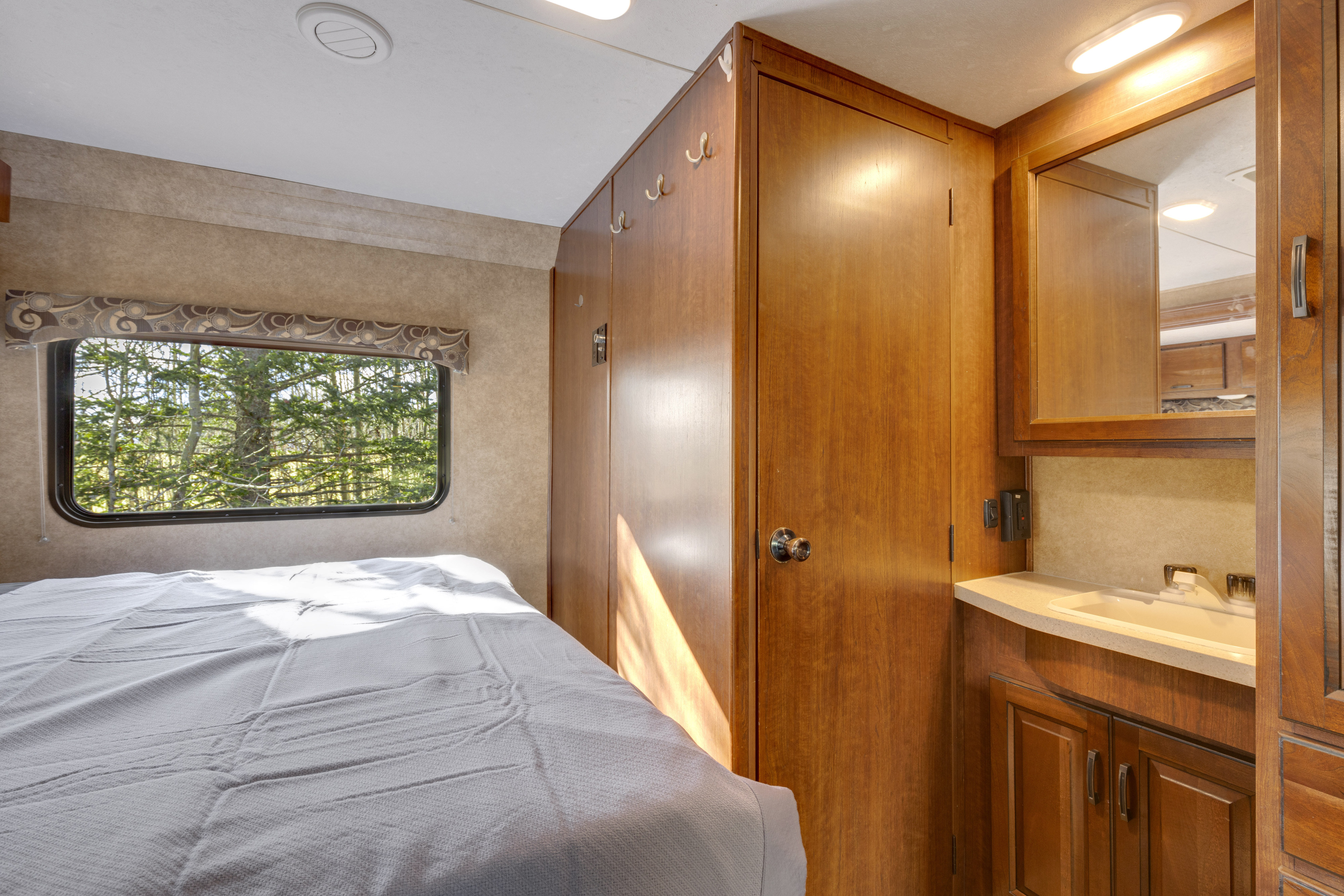 Comfortable RV rental bedroom featuring a bed, window with nature view, and compact vanity. Perfect for your next adventure.. Forest River Sunseeker 2014
