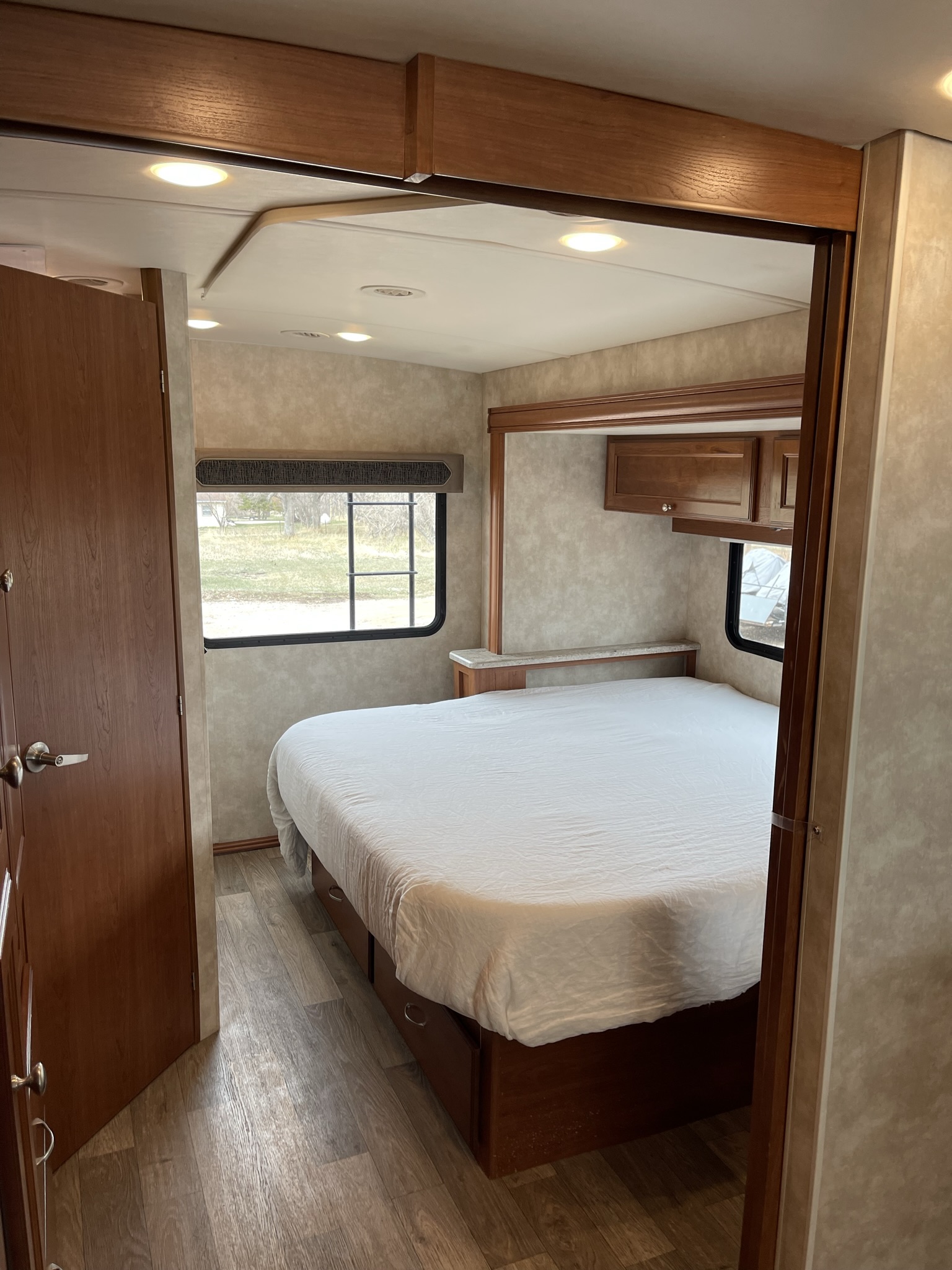 Cozy RV rental bedroom featuring a large white bed, wood laminate flooring, recessed lighting, and a view from the window.. Winnebago Vista 2018