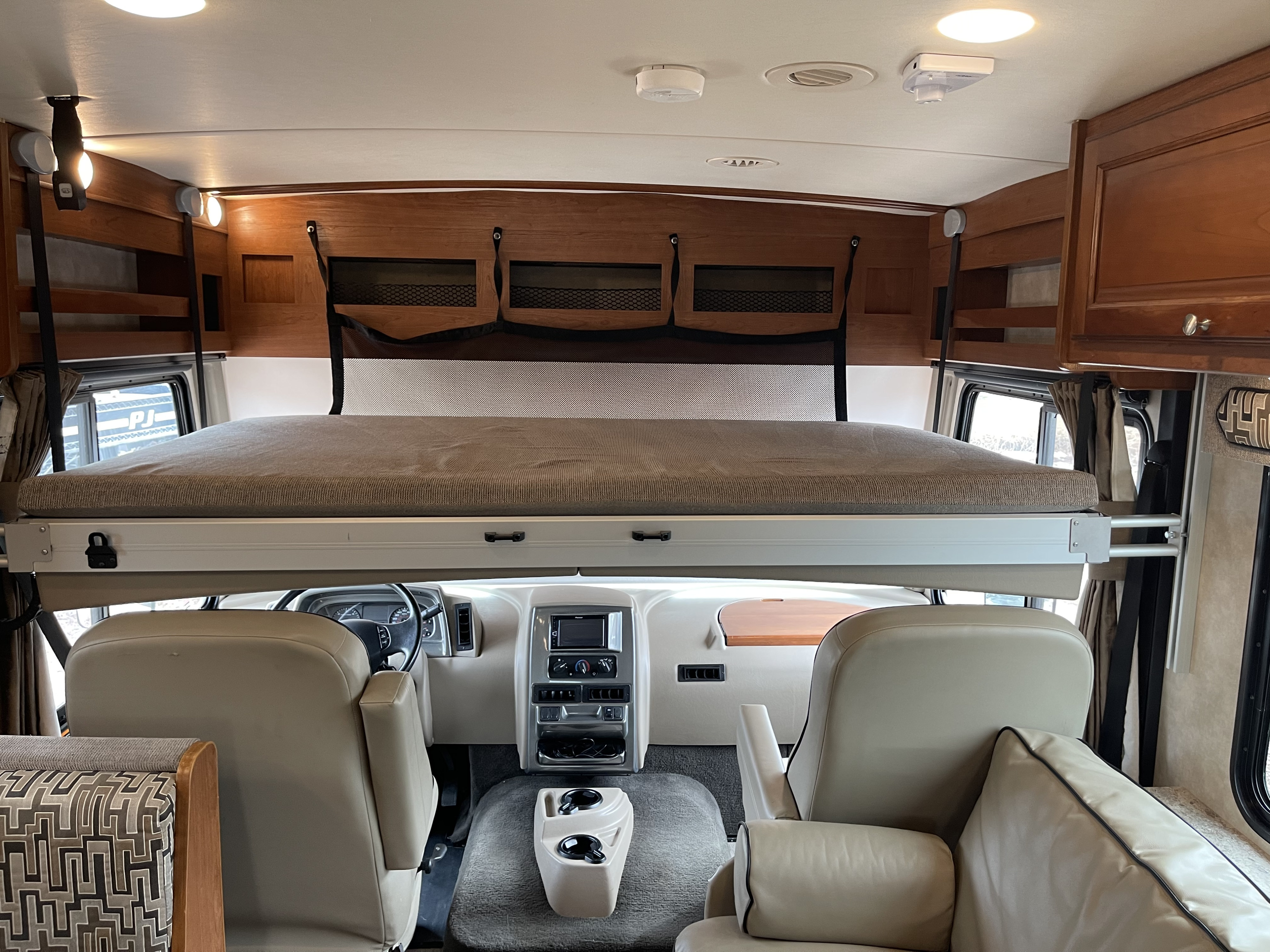 Spacious RV rental interior featuring a cozy cab-over bunk bed, front cockpit, and wooden cabinetry.. Winnebago Vista 2018