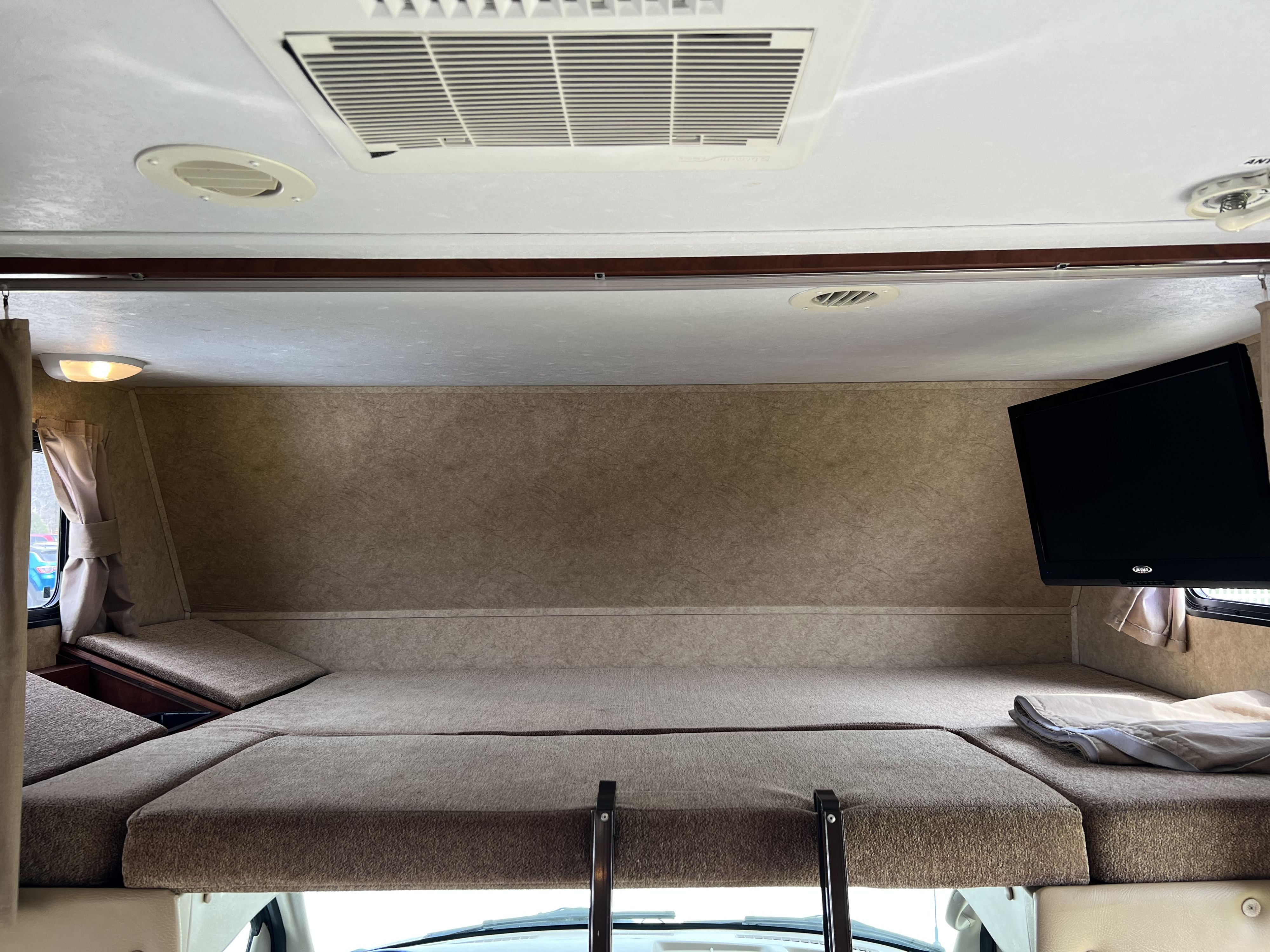 Spacious cab-over bunk bed in an RV rental, featuring a mounted TV, AC, and cozy sleeping area for comfort.. Forest River Sunseeker LE 2013