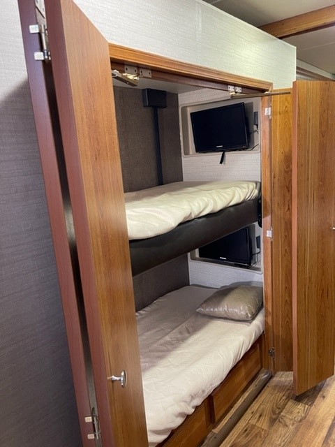Opened doors reveal compact RV rental bunk beds, each with a TV. Ideal for family adventures, offering comfortable sleeping and entertainment.. Jayco Precept 2017
