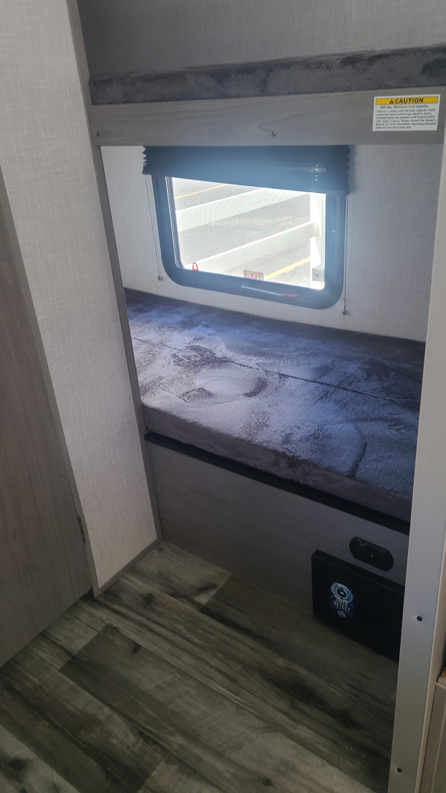 This RV rental shows a compact interior with stacked bunk beds, a window, and wood-look flooring. Includes safety labels.. Dutchman Coleman Lantern LT 17B 2022