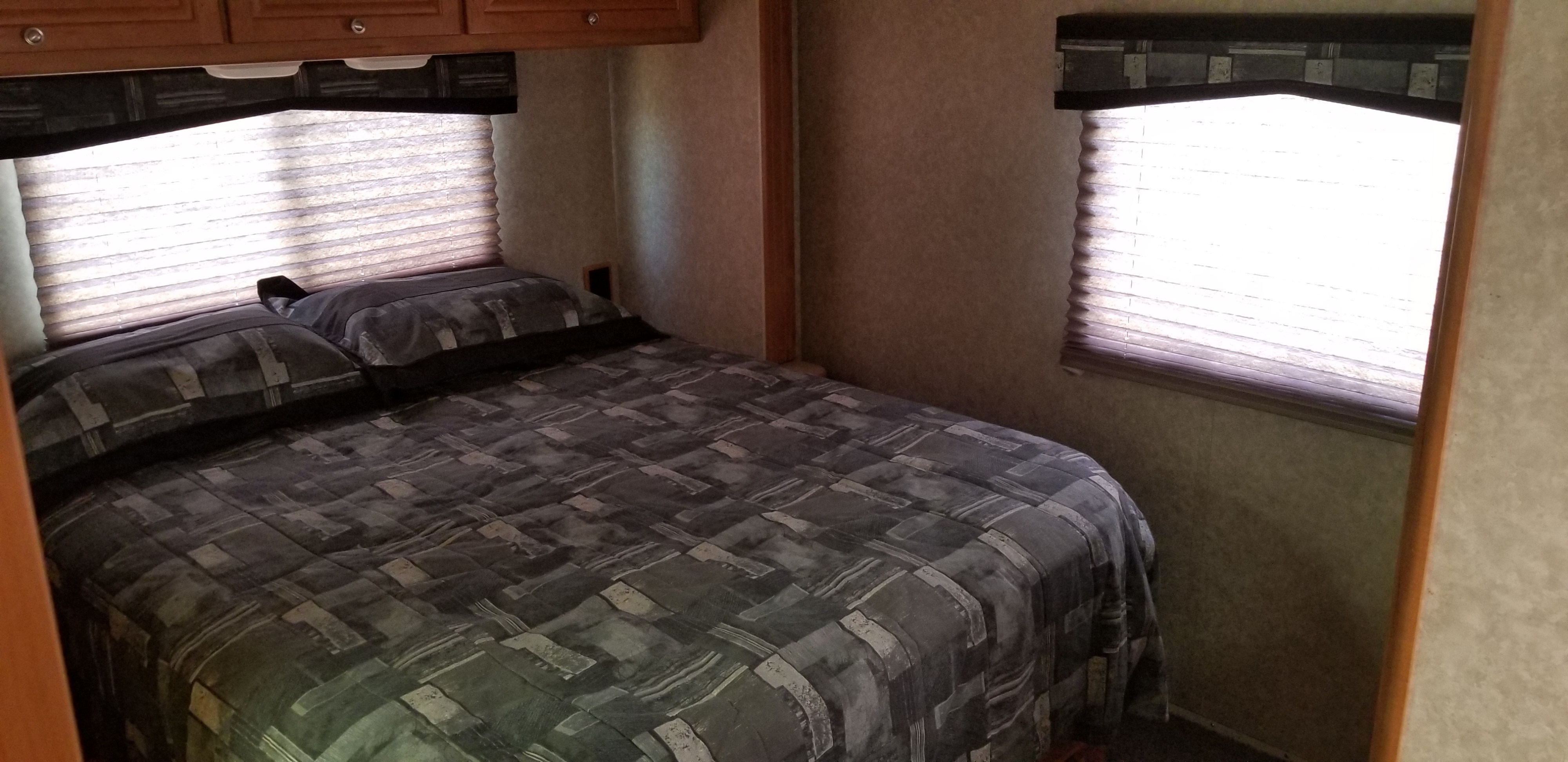Cozy RV rental bedroom with a patterned bed, blinds on windows, and overhead cabinets.. Winnebago Access 2009