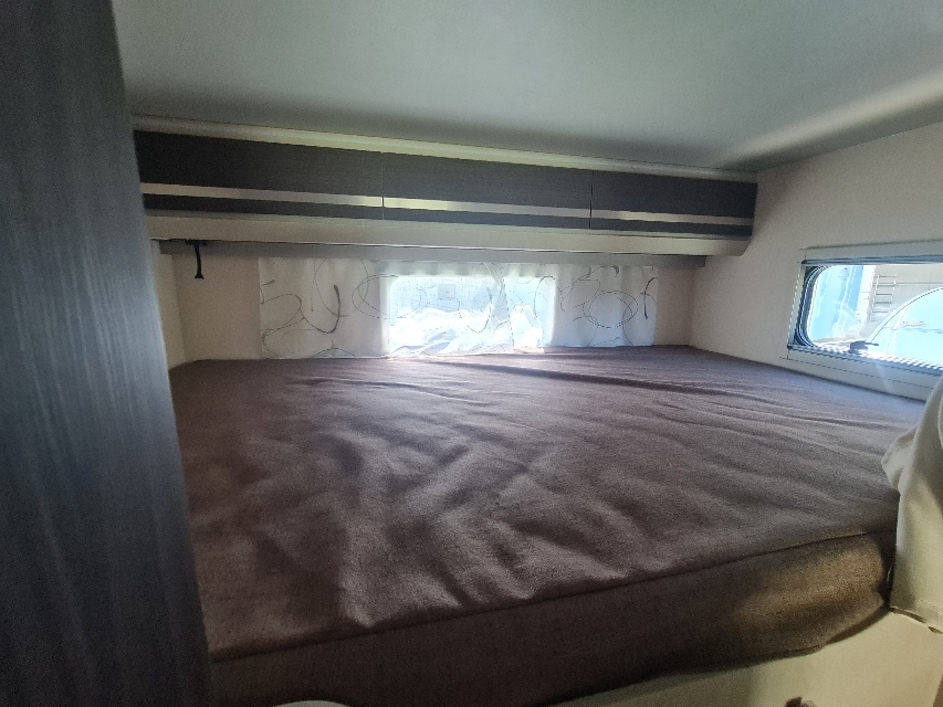 Comfortable RV rental sleeping area featuring a plush bed, overhead cabinets, and bright window with curtains.. Rimor Seal 5 2022