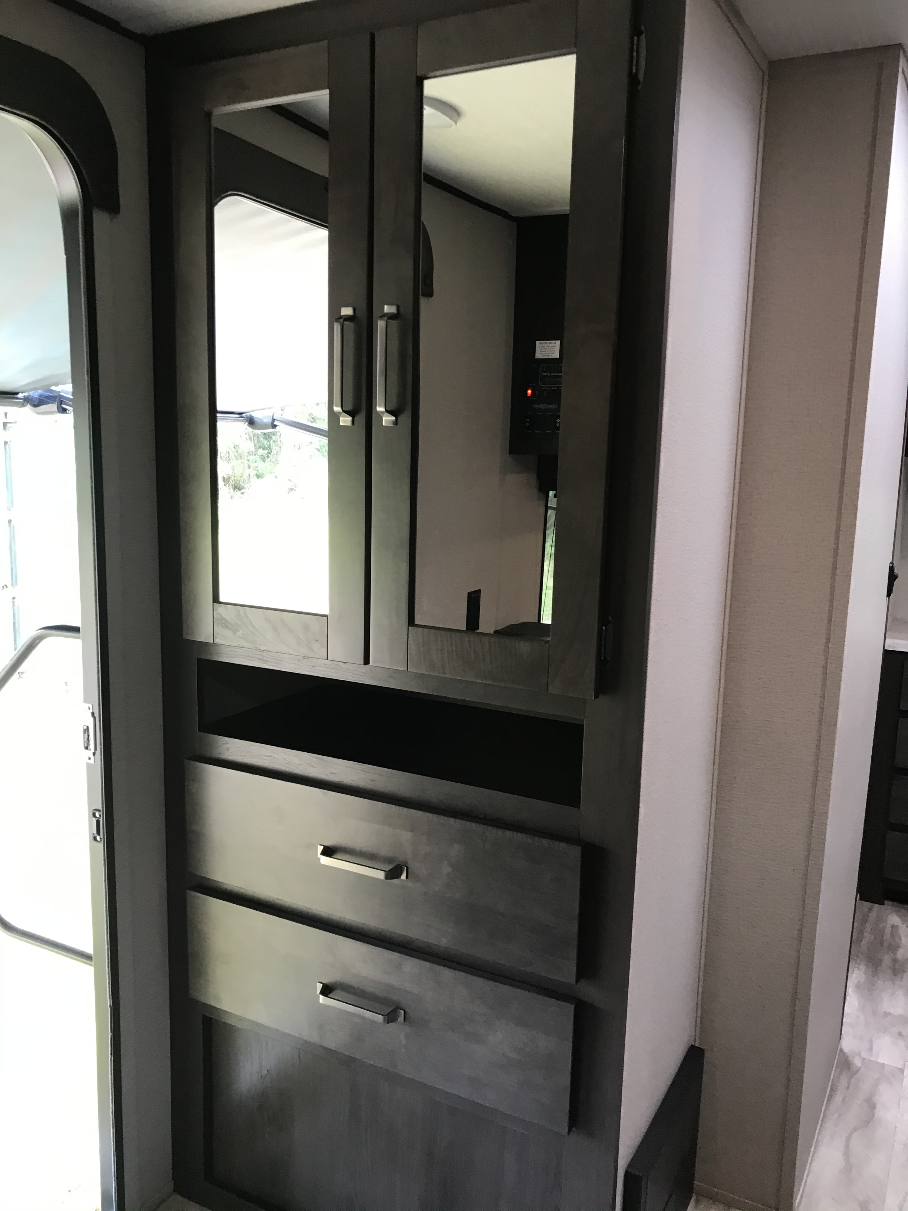 RV rental: Sleek dark cabinet with mirrored upper doors, open shelf, and two drawers, providing storage near the main entrance.. Grand Design Transcend Xplor 2021