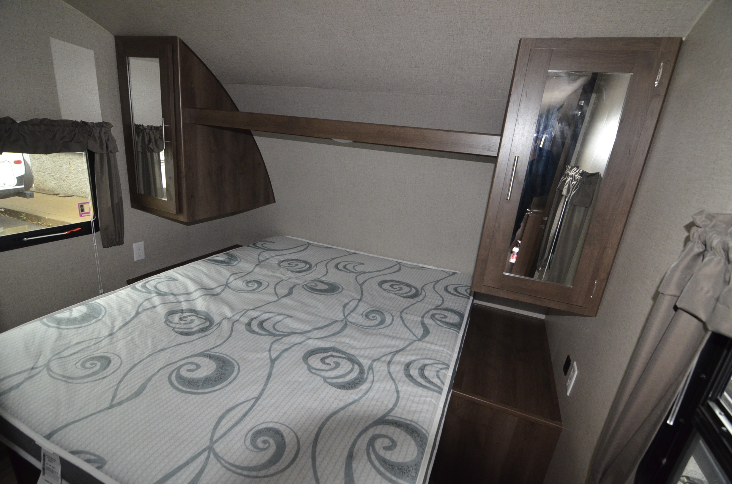 Compact RV rental bedroom featuring a patterned bed, mirrored overhead cabinets, and a side window, for cozy travel.. Shasta 26BH 2019
