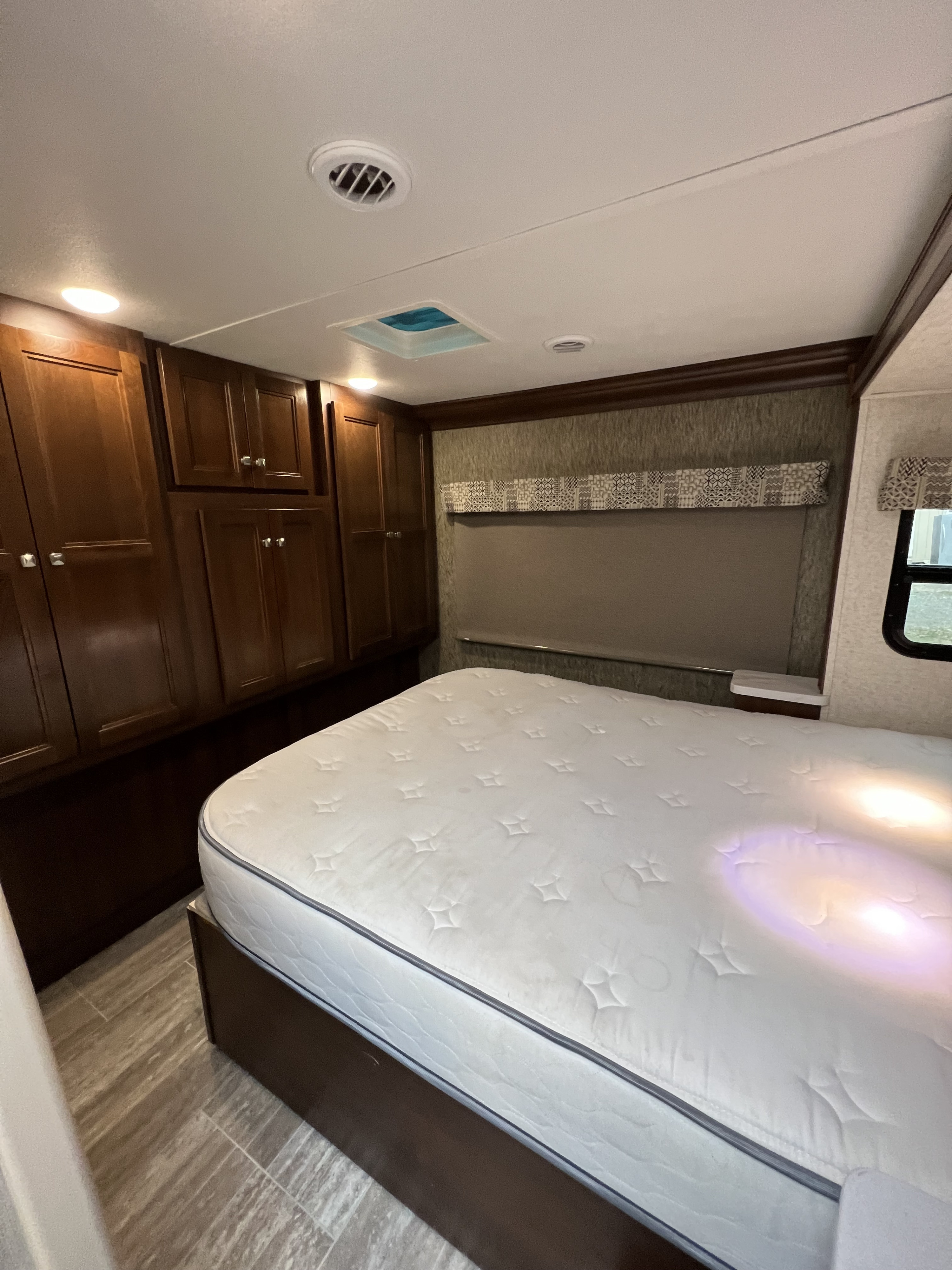 Cozy RV rental bedroom featuring a large mattress, ample dark wood storage cabinets, window, and modern lighting.. Forest River Forester 2019