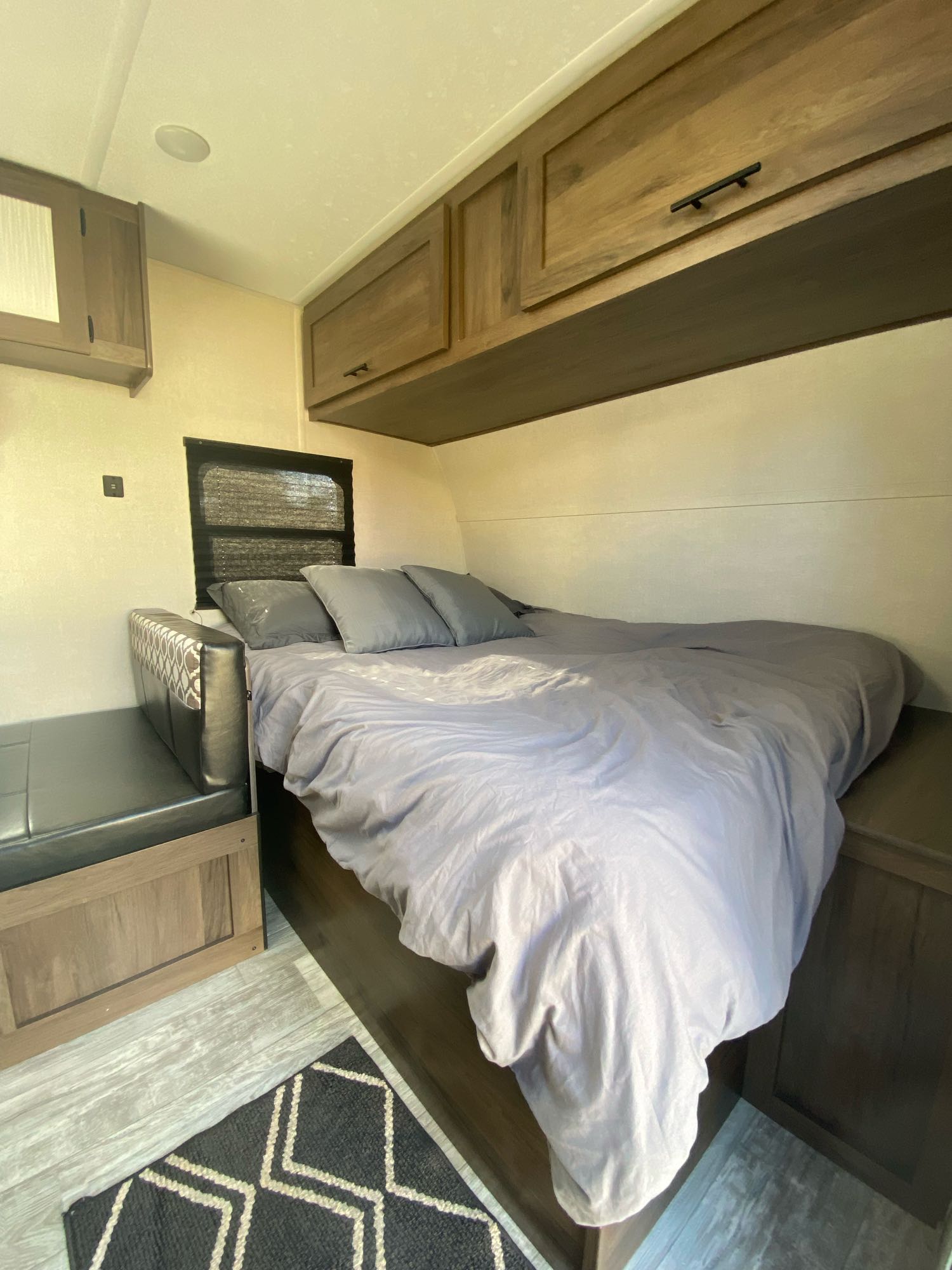 An RV rental interior featuring a cozy bed with gray bedding, overhead cabinets, and a bench seat.. Prime Time Avenger 2021