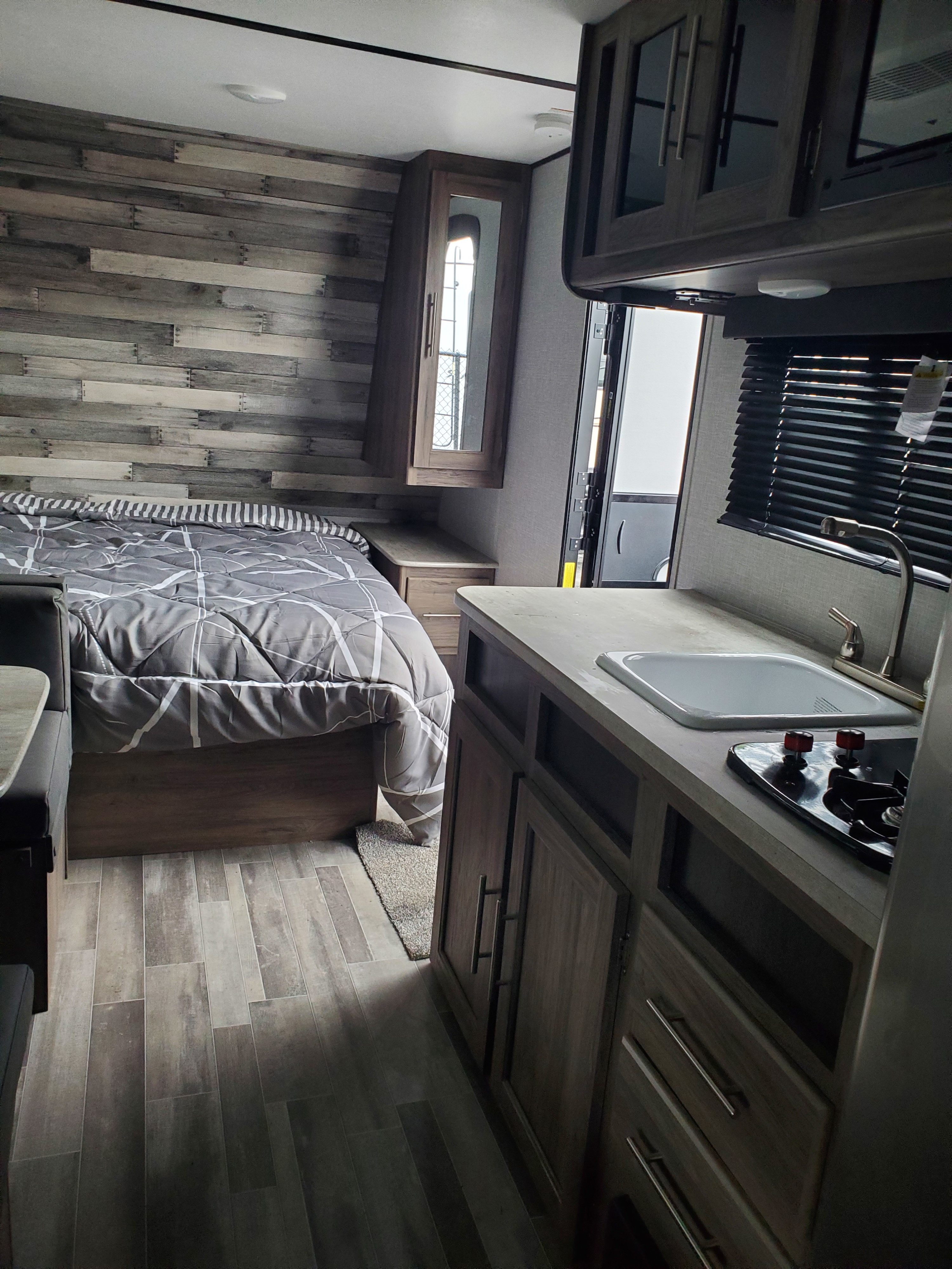Compact RV rental interior featuring a cozy bedroom area with rustic walls, and a well-equipped kitchen with sink and stove.. Crossroads RV Zinger 2021