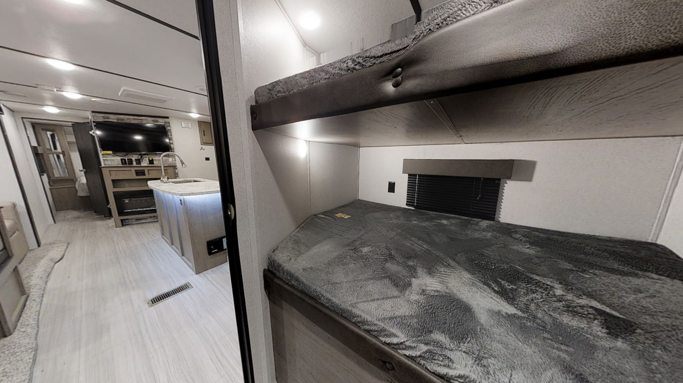 RV rental interior: Right shows bunk beds with lights & window. Left reveals kitchen island, sink, and living area with TV.. Keystone RV Hideout 2022