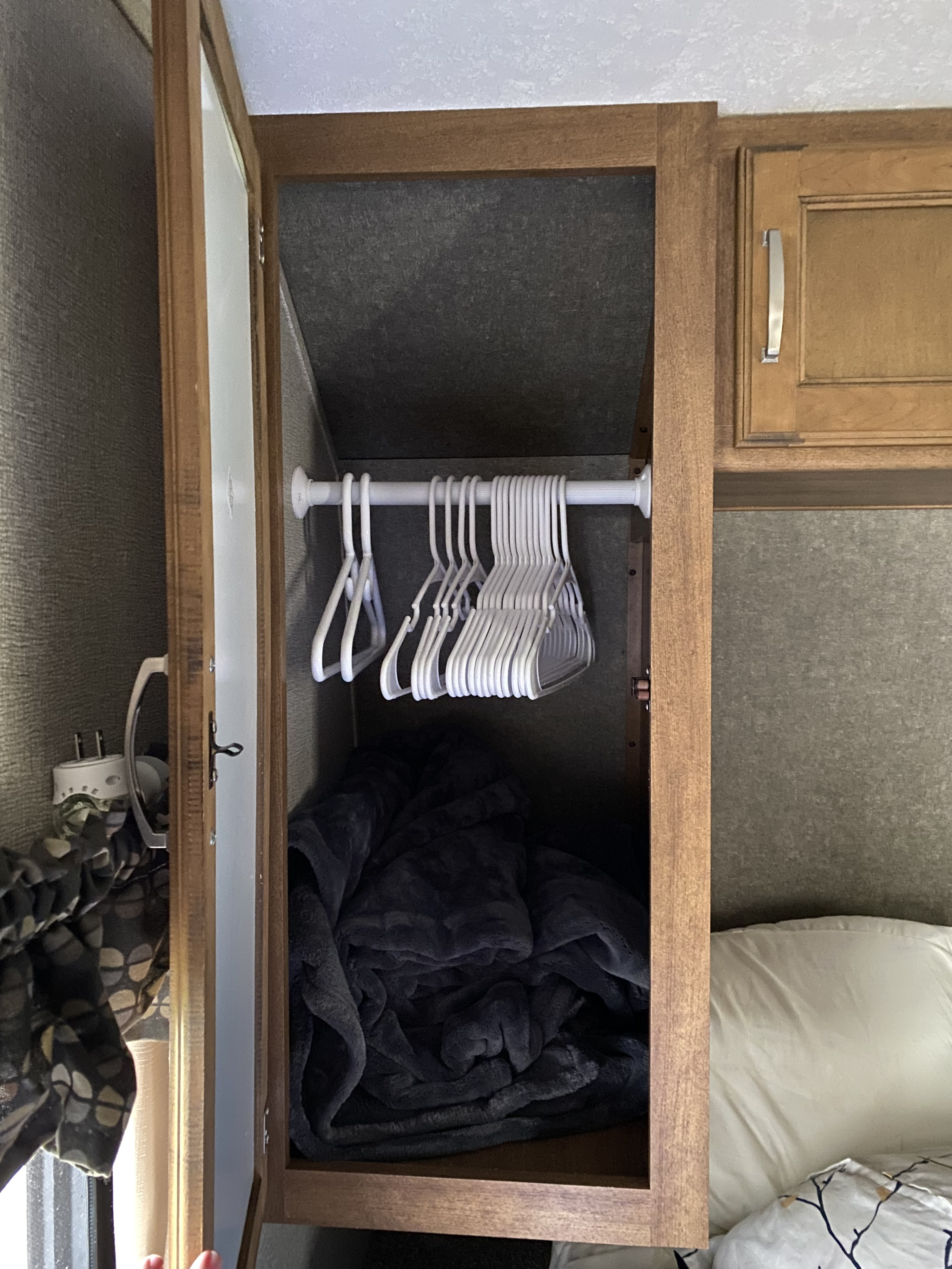 Open closet in an RV rental bedroom, showing white hangers on a rod and a dark blanket below. Efficient RV storage.. Keystone RV Springdale 2017