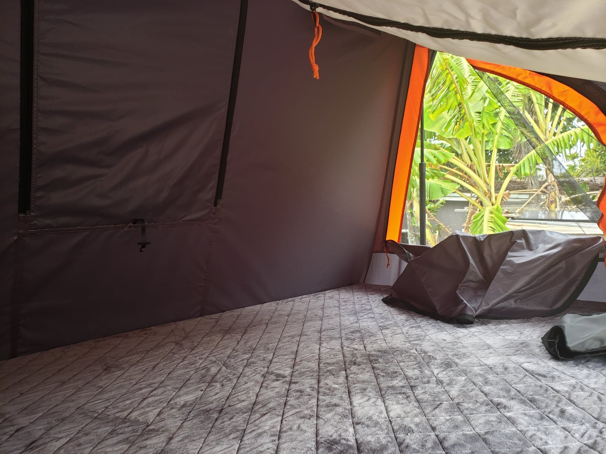 Interior of an RV rental: a cozy tent space with quilted mattress, window view of lush trees, perfect for camping.. Nissan Xterra 4x4 2012
