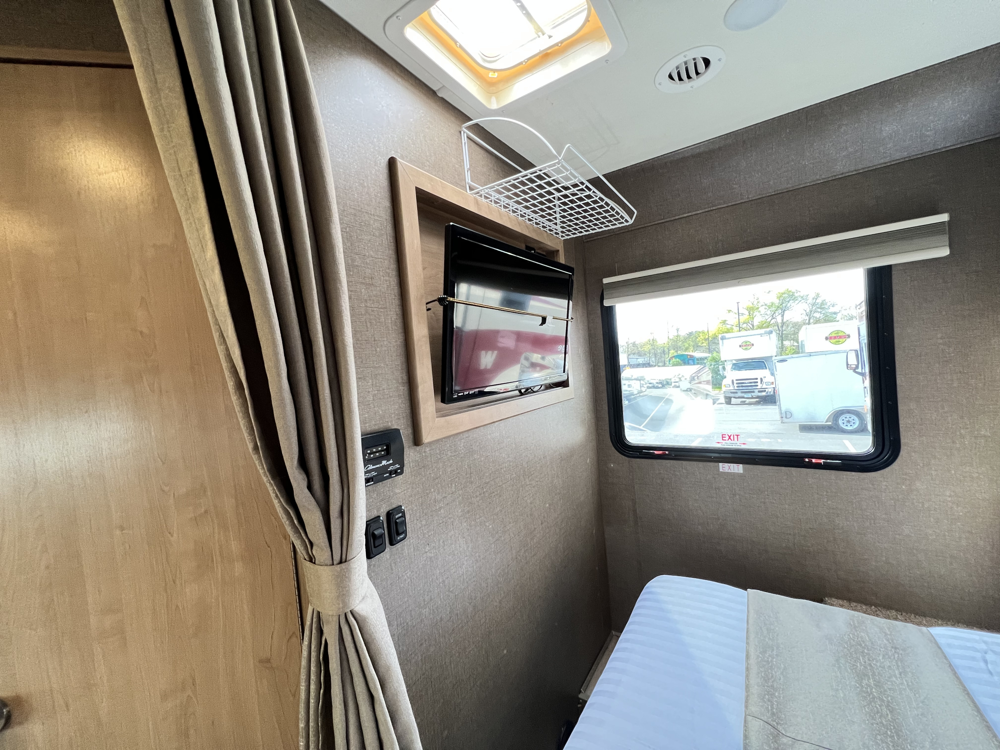 This RV rental offers a compact bedroom with a bed, wall-mounted TV, and window view of a parking lot.. Thor Freedom Elite 2018