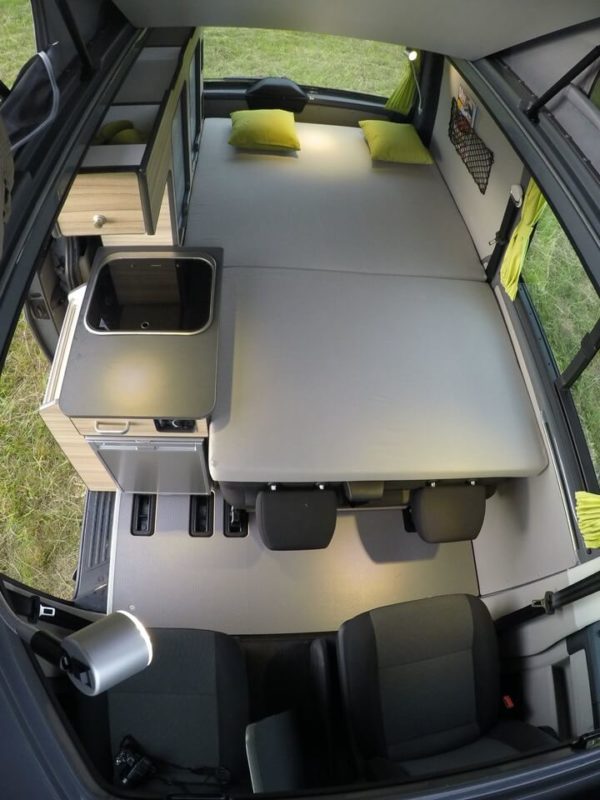 Compact RV rental interior: bed, kitchen, and seats. This functional camper van layout is ready for your next adventure.. Volkswagen Transporter T6.1 2022