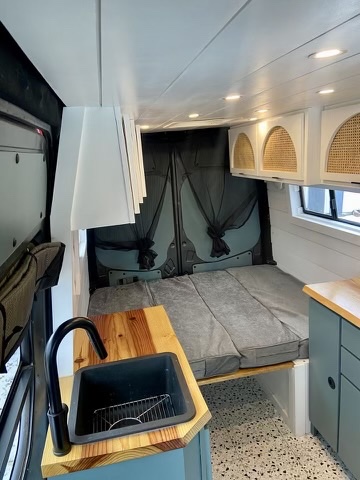 Stylish custom RV rental interior with a bed, sink, wooden counter, and cane-front cabinets for mobile living.. Freightliner Sprinter 2011