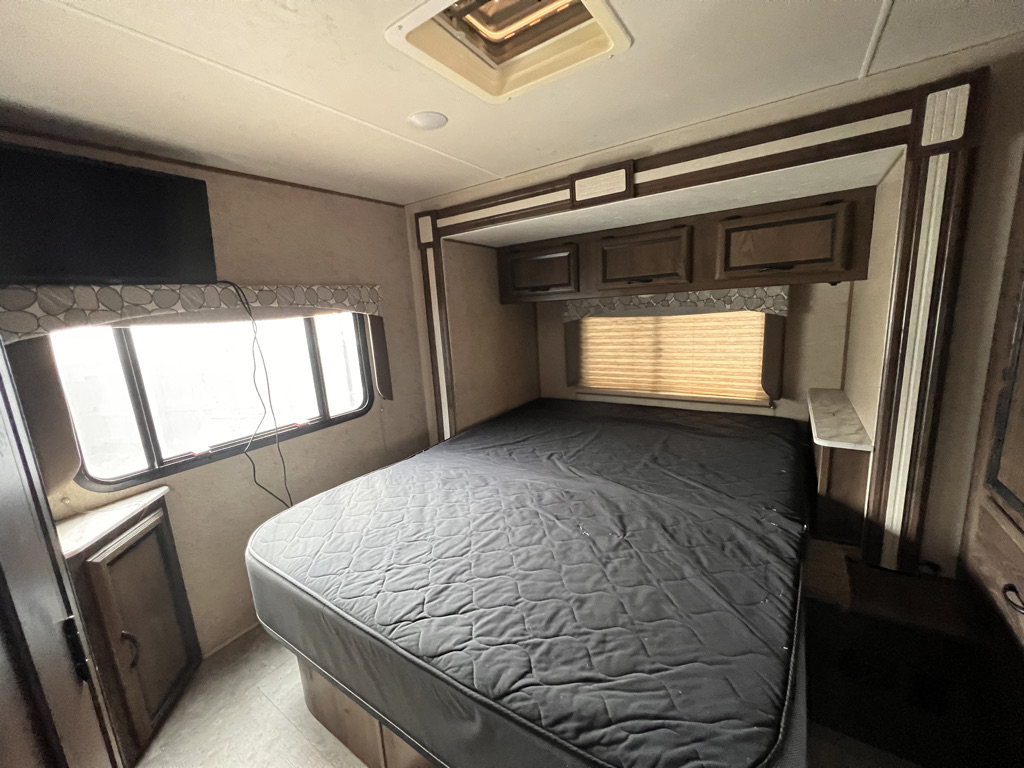 Cozy RV rental bedroom with queen bed, TV, window, and overhead storage. Ideal for your next travel adventure.. Coachmen Freelander 2019