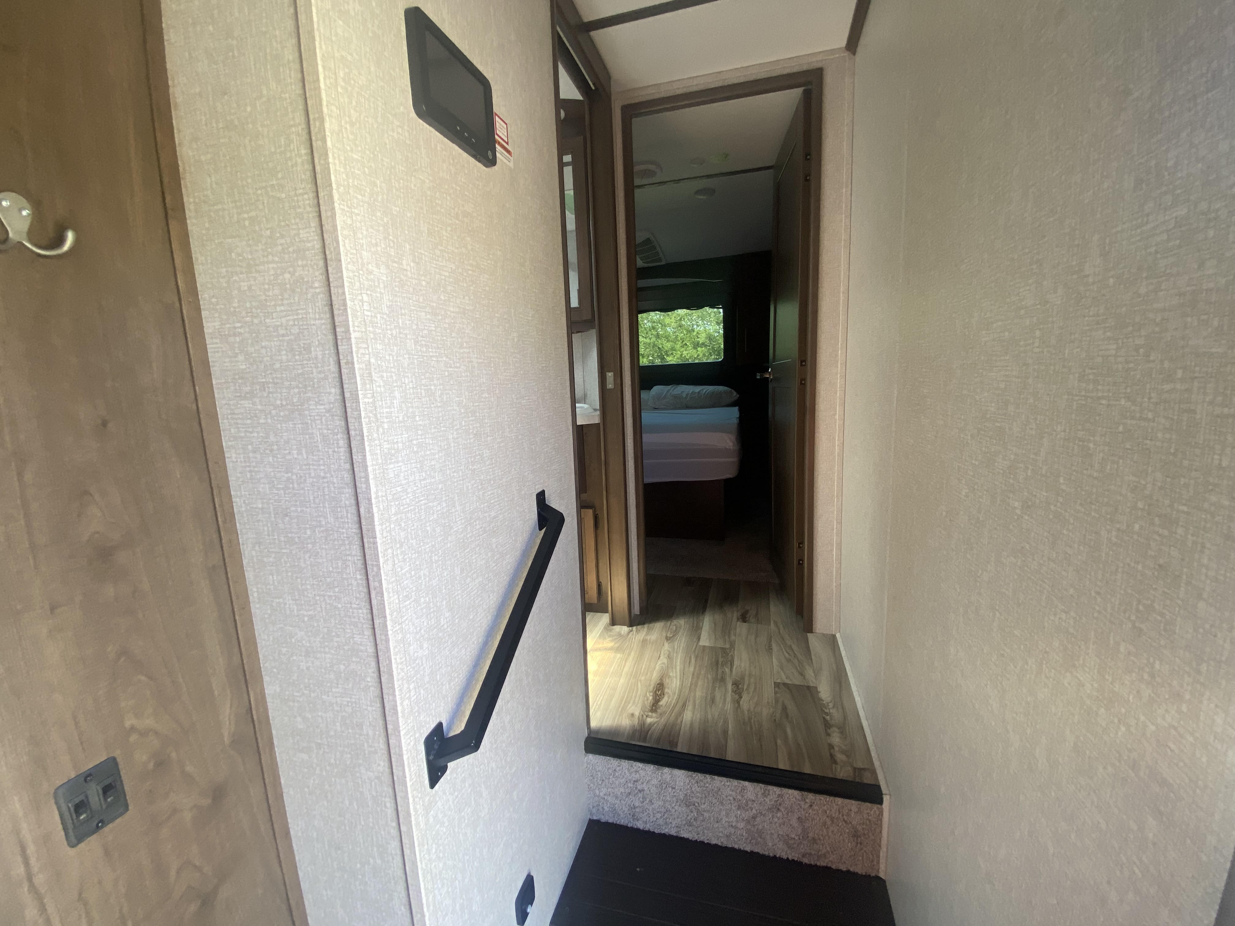 Inside an RV rental: Looking down stairs into a hallway with a bedroom visible, featuring a handrail and control panel.. Keystone RV Cougar 2021