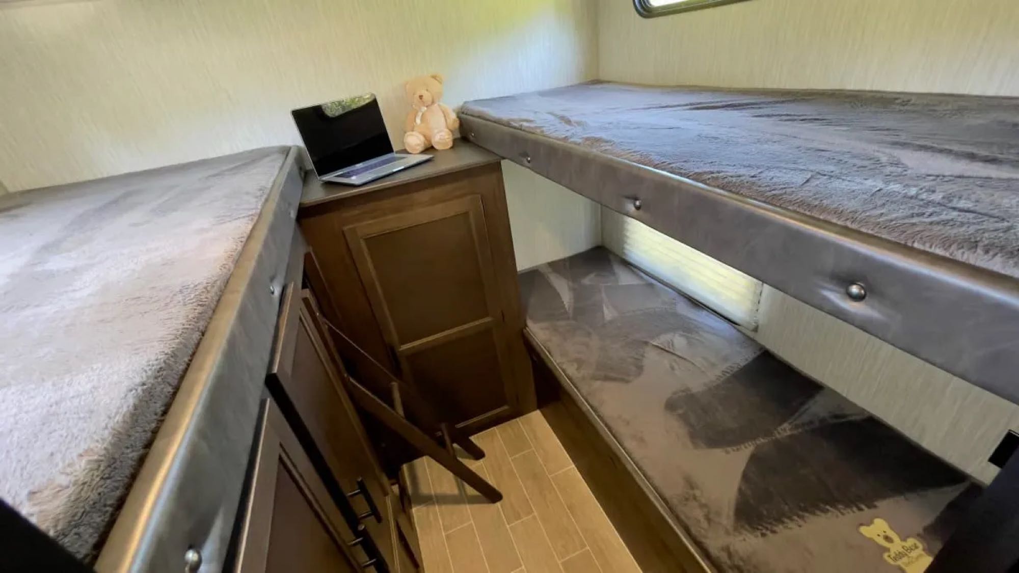 RV rental bunk room showing three beds, a laptop, and a teddy bear. Plush grey bedding and wood-paneled storage.. Forest River Cherokee Grey Wolf 2020