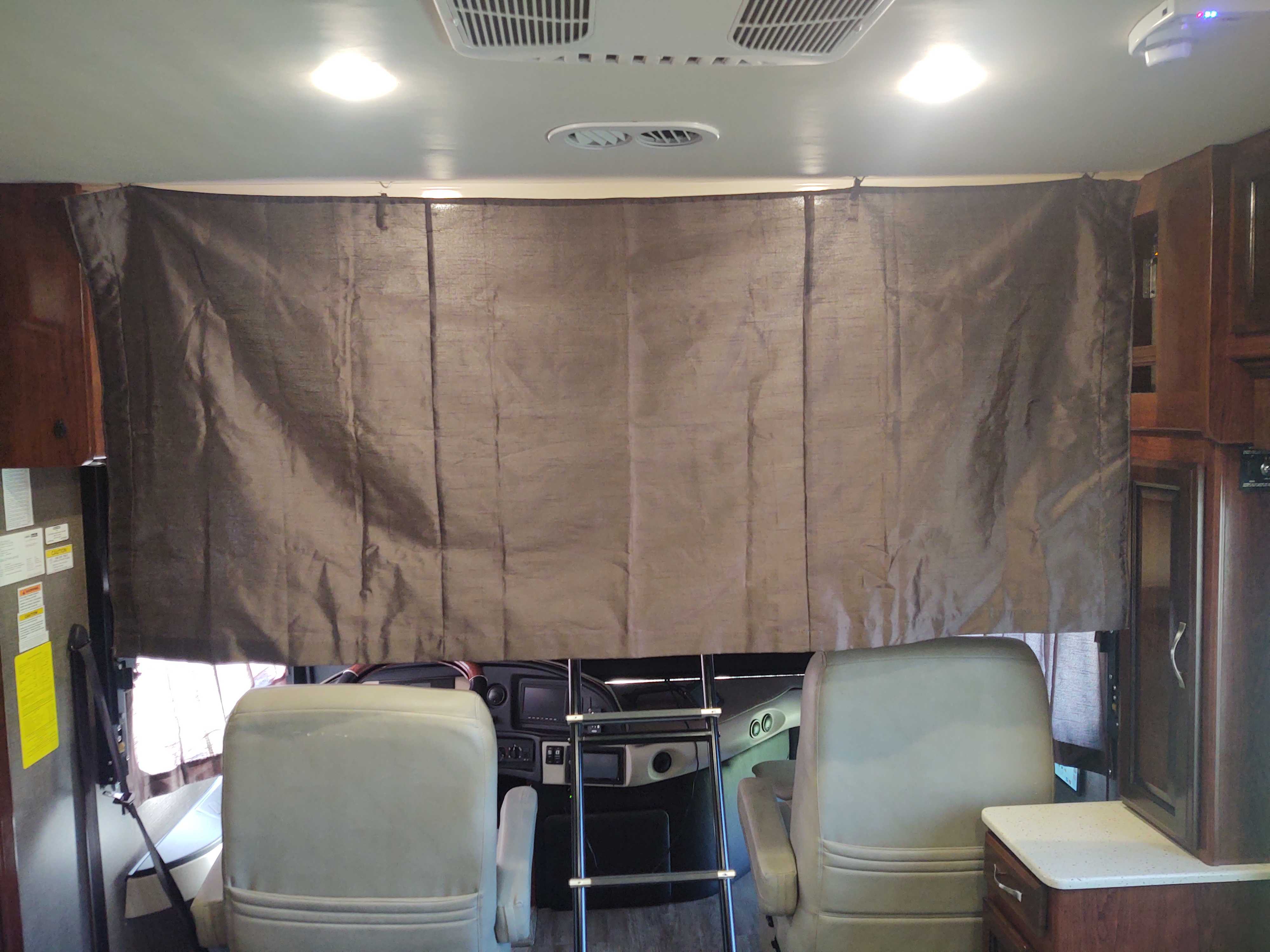 Interior of an RV rental with a large brown privacy curtain drawn across the front. Two light-colored seats face the dashboard.. Fleetwood Pace Arrow 2018