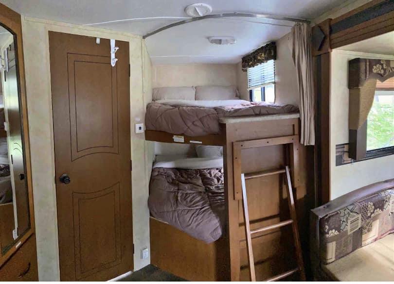 RV rental interior: cozy bunk beds with bedding, a ladder for the top bunk, and a brown door on the left side.. Keystone RV Springdale 2013