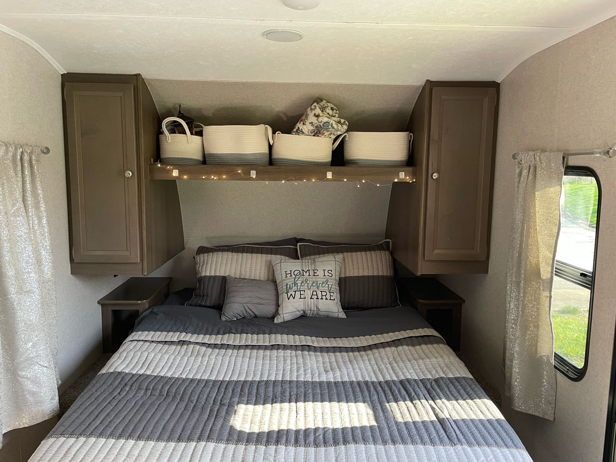 This inviting RV rental bedroom offers comfort with striped bedding, ample overhead storage, and quaint decor.. Forest River Independence Trail 2021