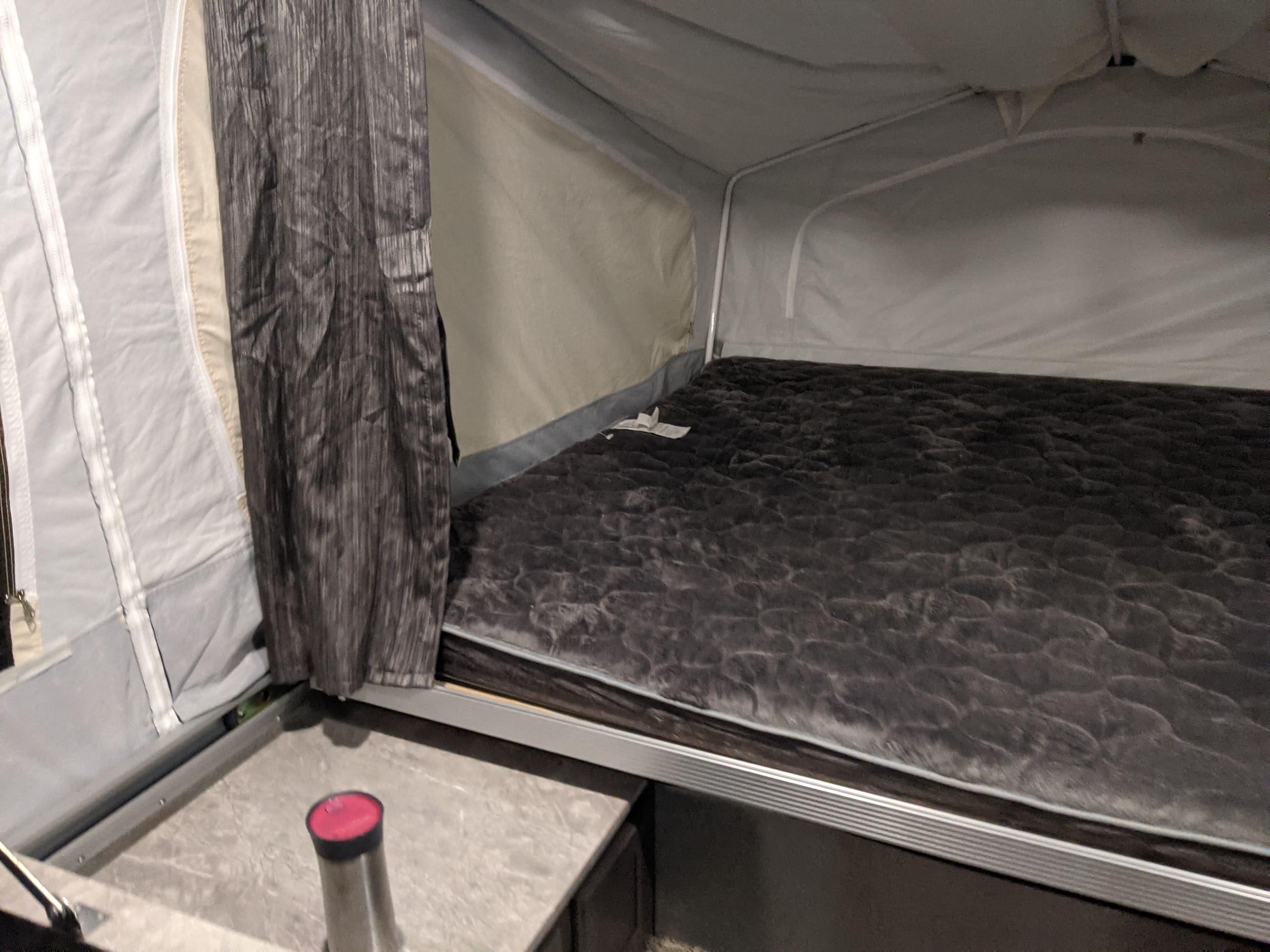 RV rental sleeping area showing a plush, dark grey mattress, canvas walls, and a patterned privacy curtain in a pop-up camper.. Forest River Rockwood Freedom 2020