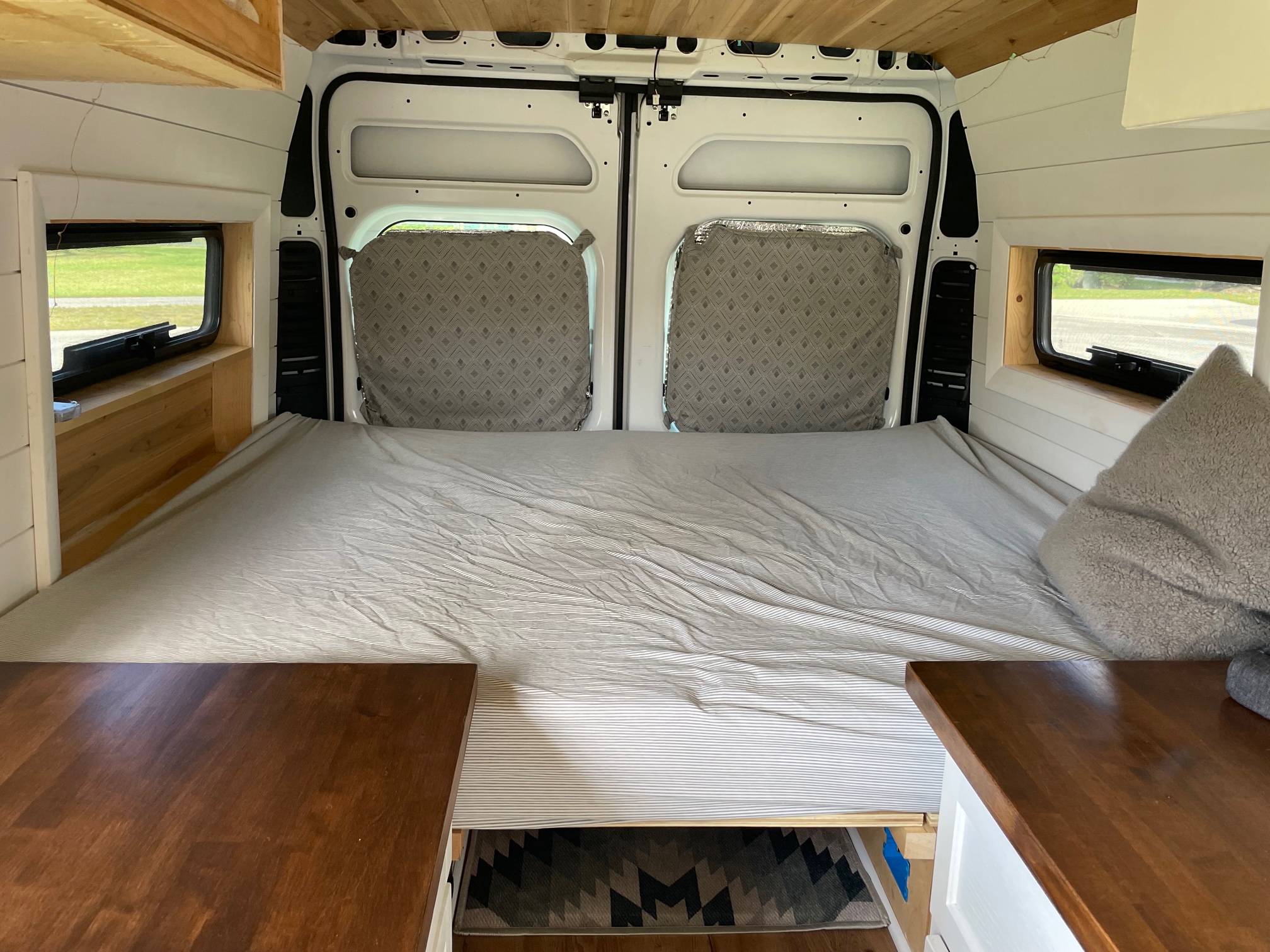 Inside an RV rental: cozy camper van sleeping area with a striped bed, side windows, and wooden interior details.. Ram Promaster 2500 High Roof 2500 159 WB 2019