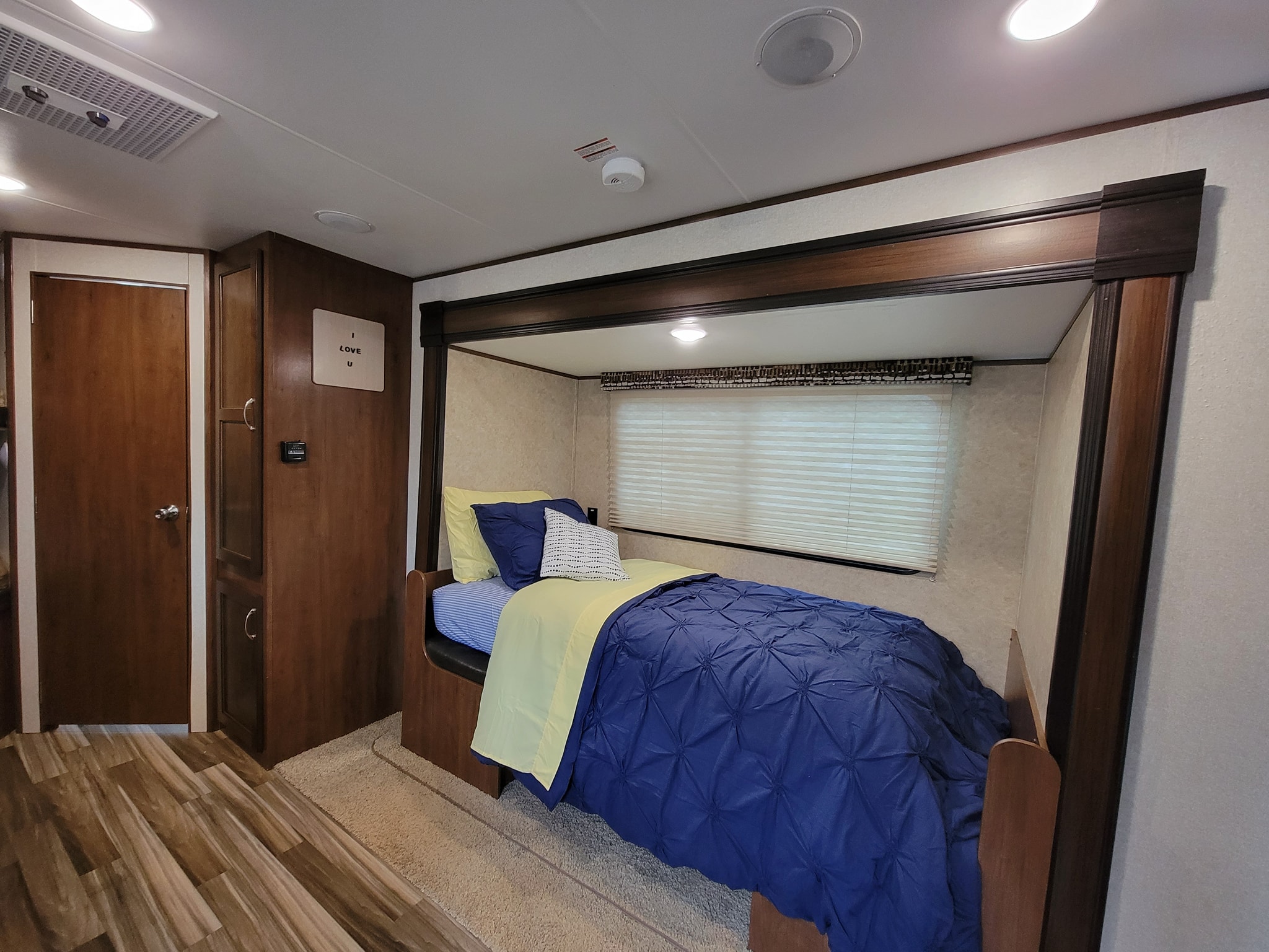 An RV rental showing a compact, cozy bunk bed with blue/yellow bedding, built-in storage, and overhead lighting.. Jayco Jay Flight SLX 2017