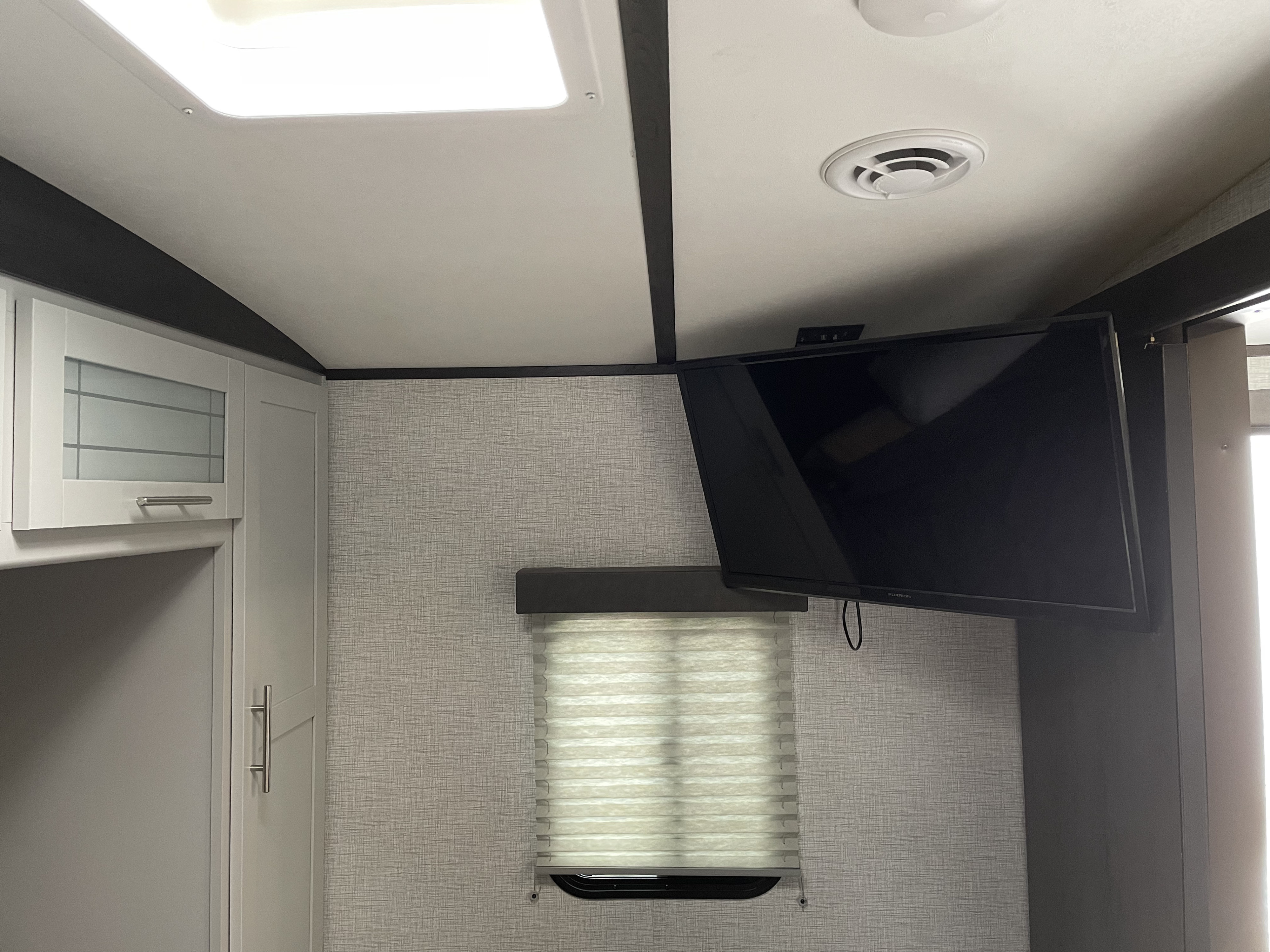 An RV rental's bright interior, showcasing a mounted TV, modern ceiling lights, cabinets, and window with blinds.. Keystone RV Bullet Ultra Lite 2021