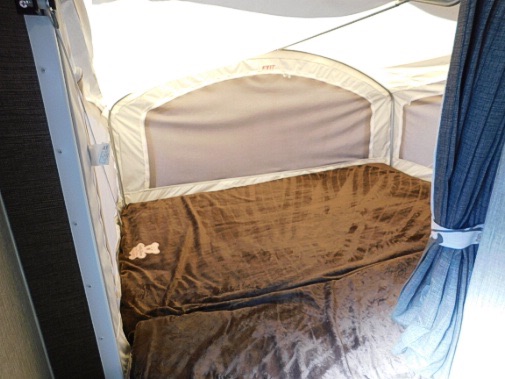 This RV rental pop-up camper features a cozy bed with a brown blanket & soft fabric walls.. Keystone RV Passport Express 2016