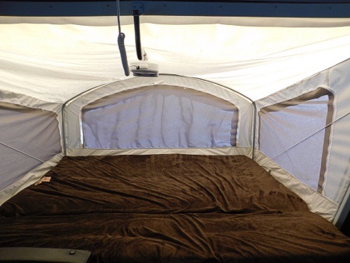 Inside an RV rental: a spacious pop-up camper bed with brown blanket & screened windows. Perfect for camping!. Keystone RV Passport Express 2016