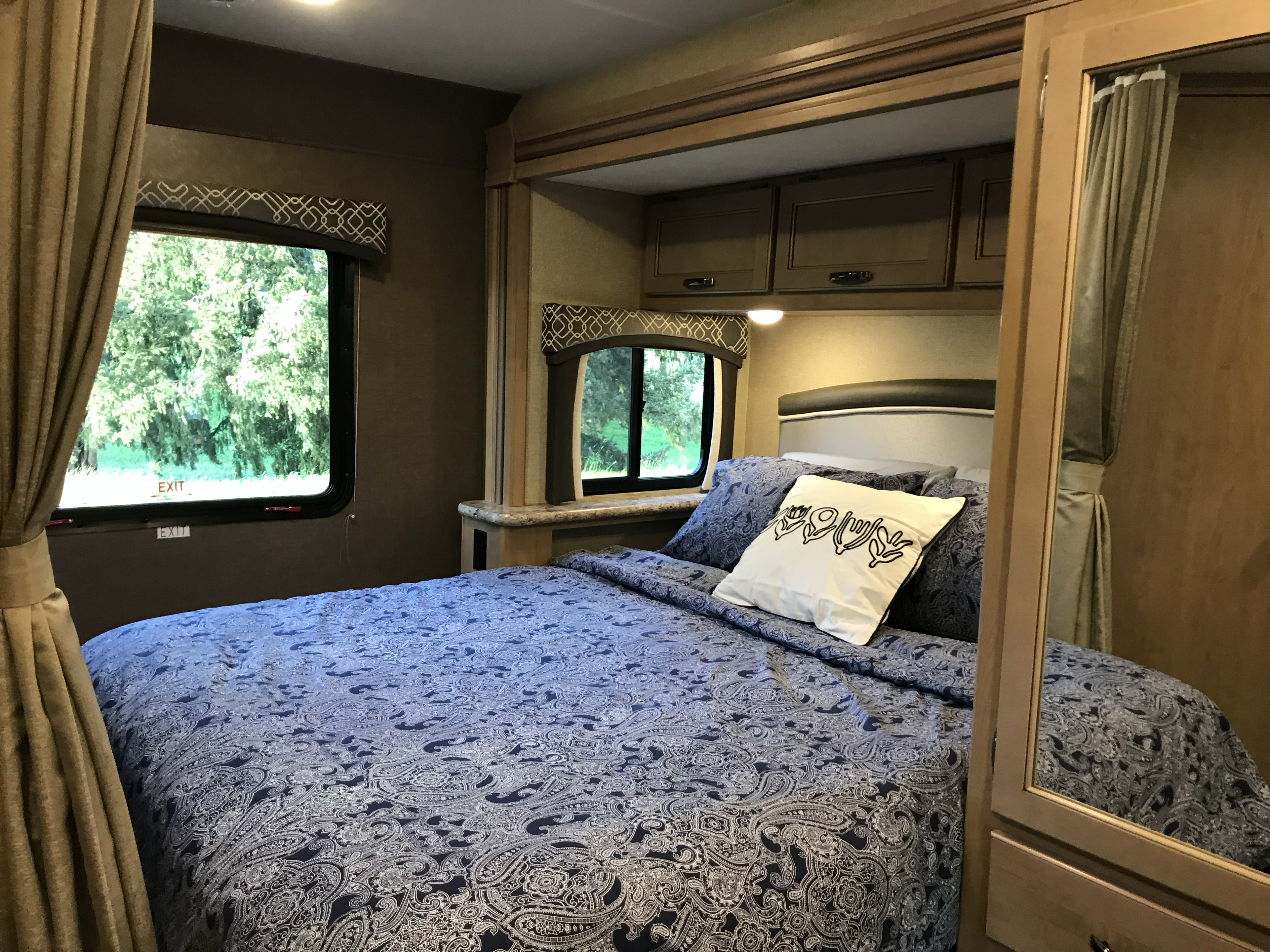 Comfortable RV rental bedroom with blue paisley bedding, windows overlooking nature, and storage cabinets.. Thor Chateau 2019
