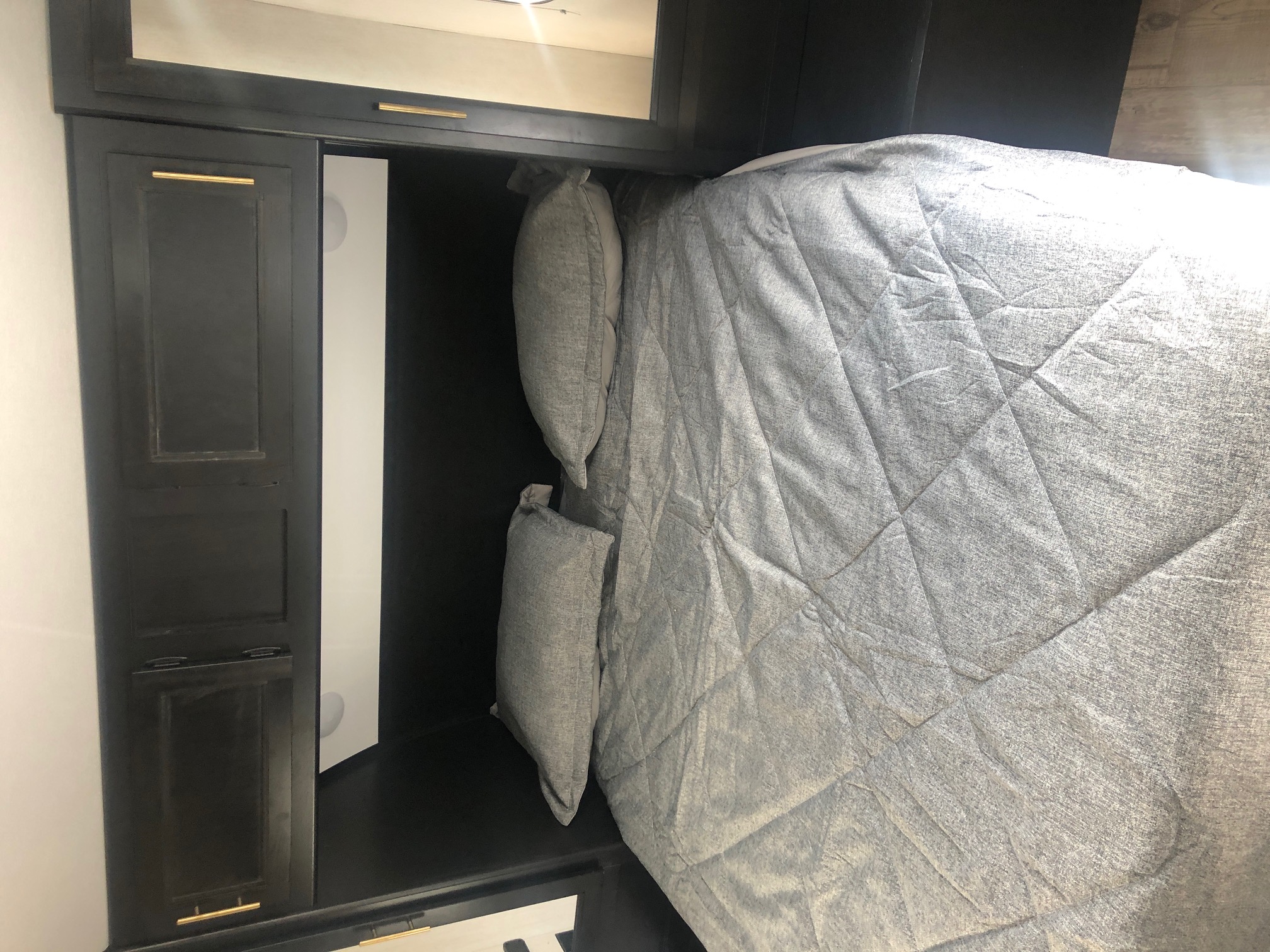 Comfortable bed area inside an RV rental, featuring gray bedding and dark cabinetry with gold handles.. Forest River Cherokee Grey Wolf 2022