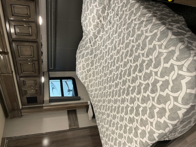 RV rental bedroom, shown vertically, with a grey patterned comforter on the bed, dark wood cabinets, and a window.. Fleetwood Frontier 2022