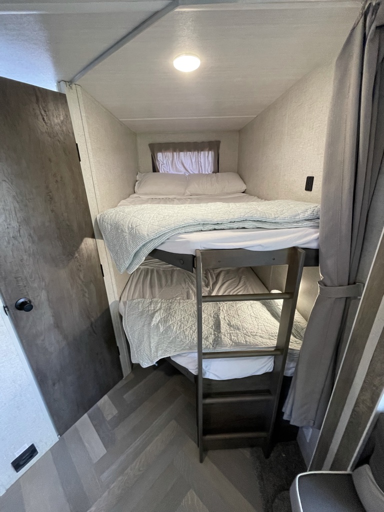 Visually impaired users: A compact sleeping area with two neatly made bunk beds, a ladder, and herringbone flooring. Great for RV rental adventures.. Forest River Other 2021