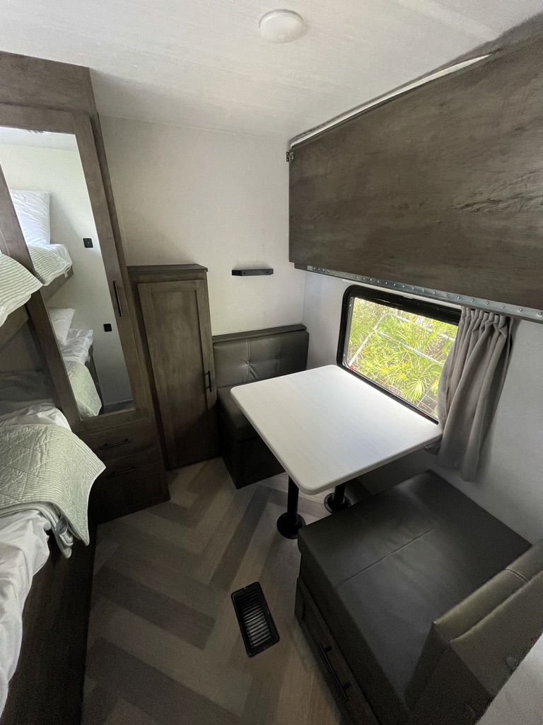 Compact RV rental interior featuring a dinette with bench seating, bunk beds, and wood-look flooring.. Forest River Salem 2021