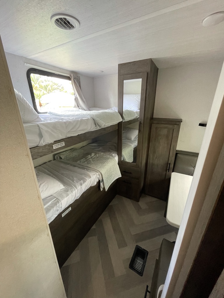 RV rental interior: two neat bunk beds, a window, mirrored cabinet, and modern herringbone flooring. Cozy camper space.. Forest River Salem 2021