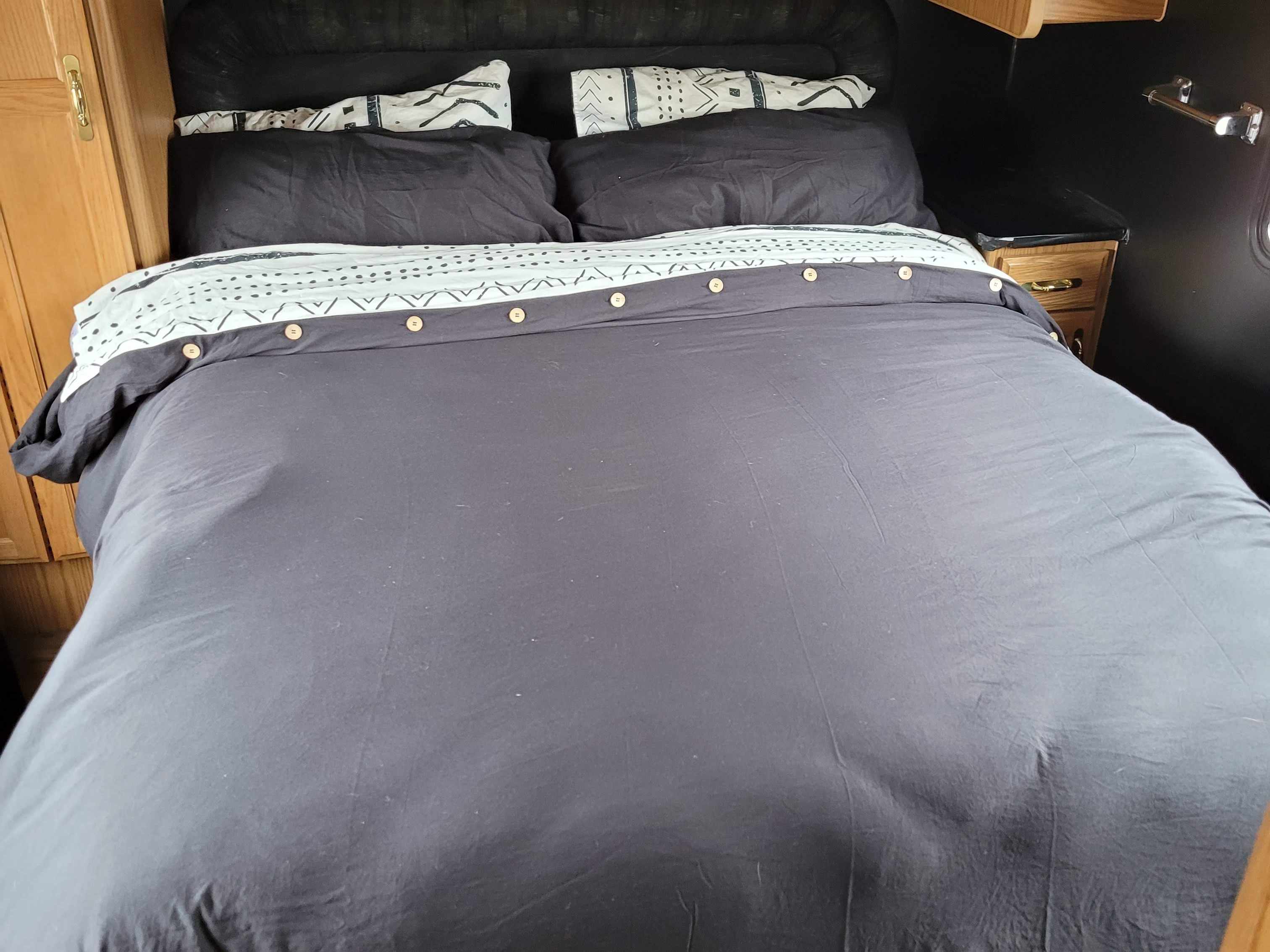 An RV rental's bed with black pillows, a duvet cover featuring a patterned black and white fold-down, and wood buttons.. Fleetwood Tioga 1996
