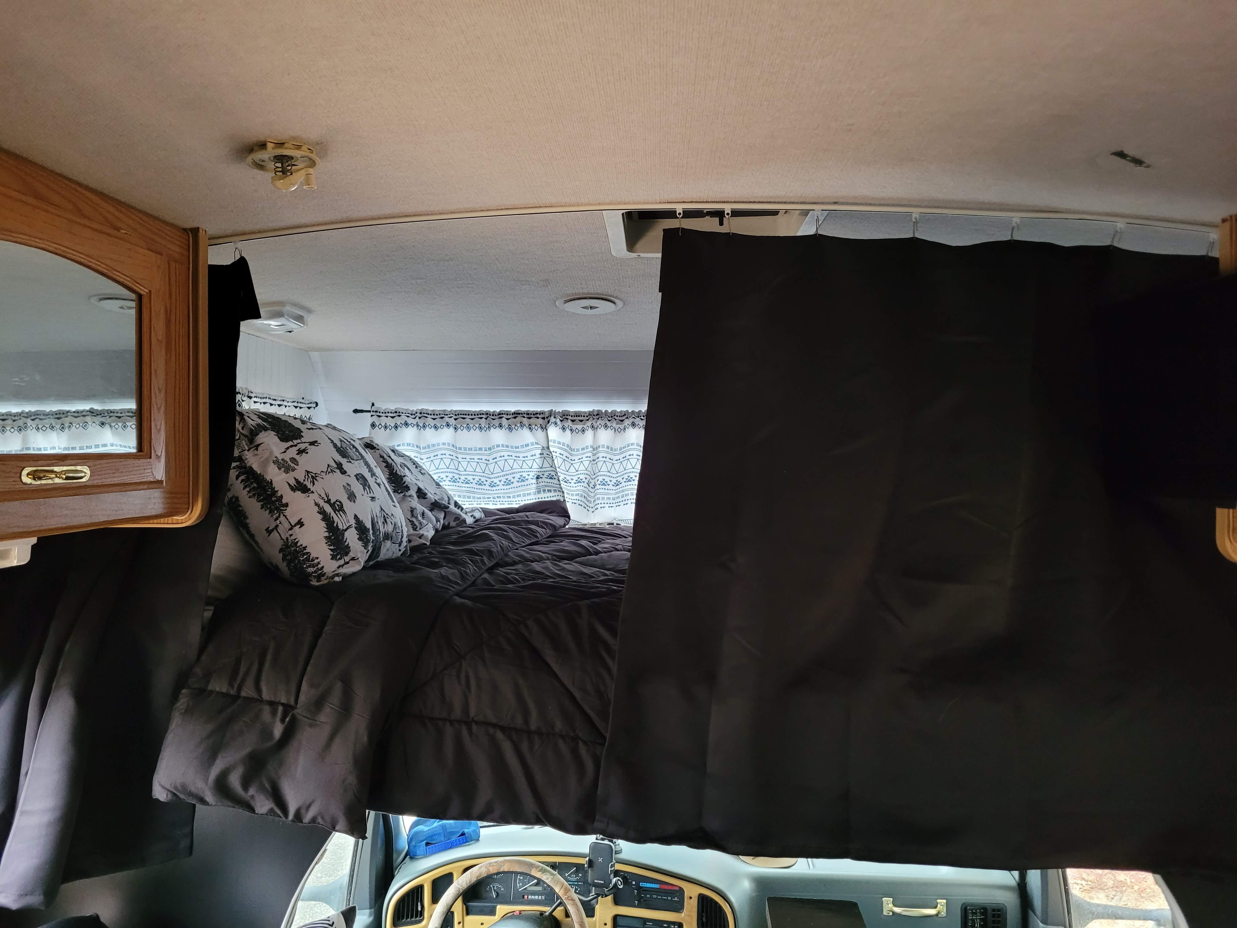 An overhead sleeping area in an RV rental, featuring a dark comforter and blackout curtains over the front cabin.. Fleetwood Tioga 1996