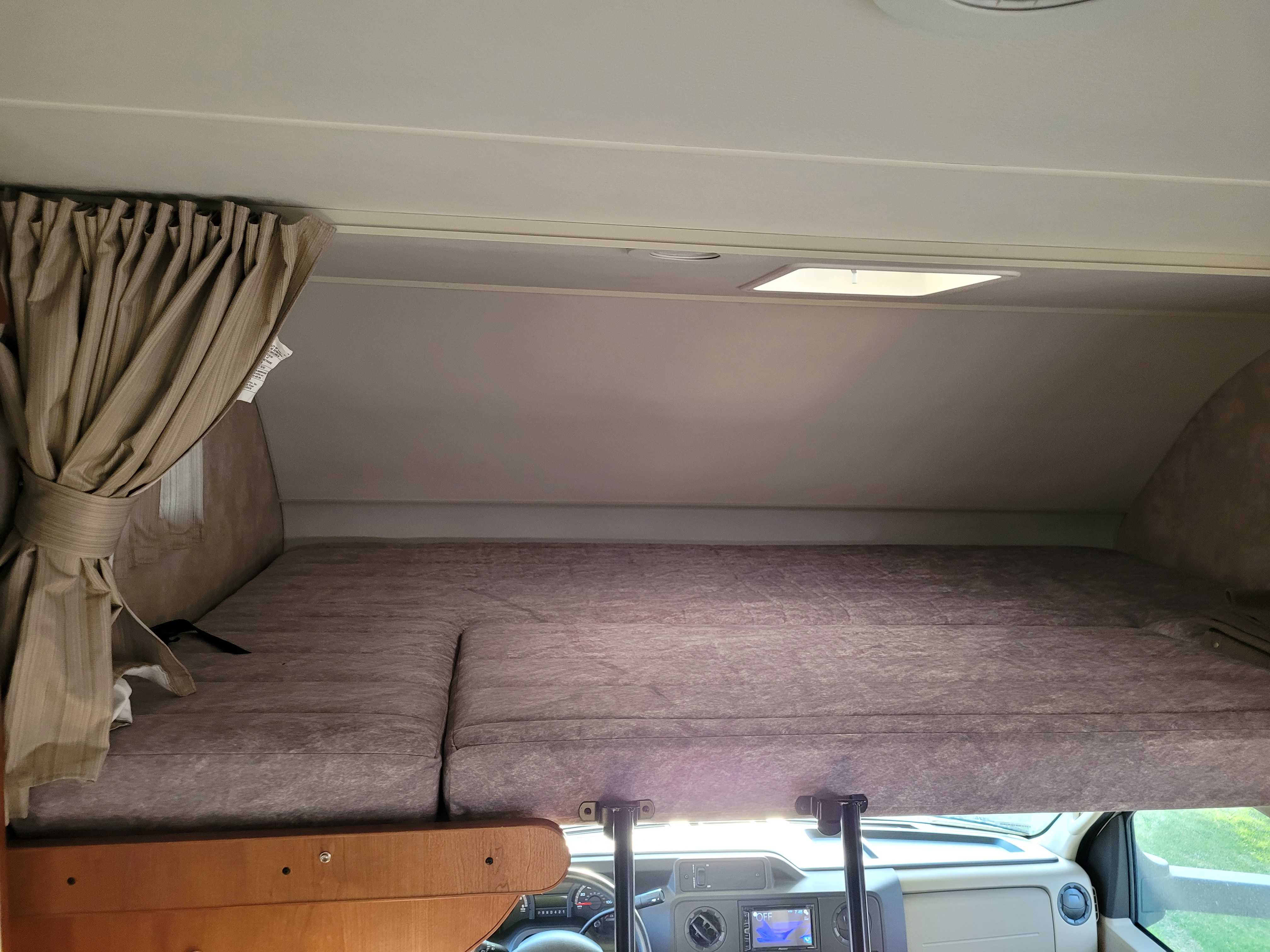 RV rental's cab-over bunk, featuring a comfortable mattress, privacy curtain, and ceiling light.. Winnebago Minnie Winnie 2018