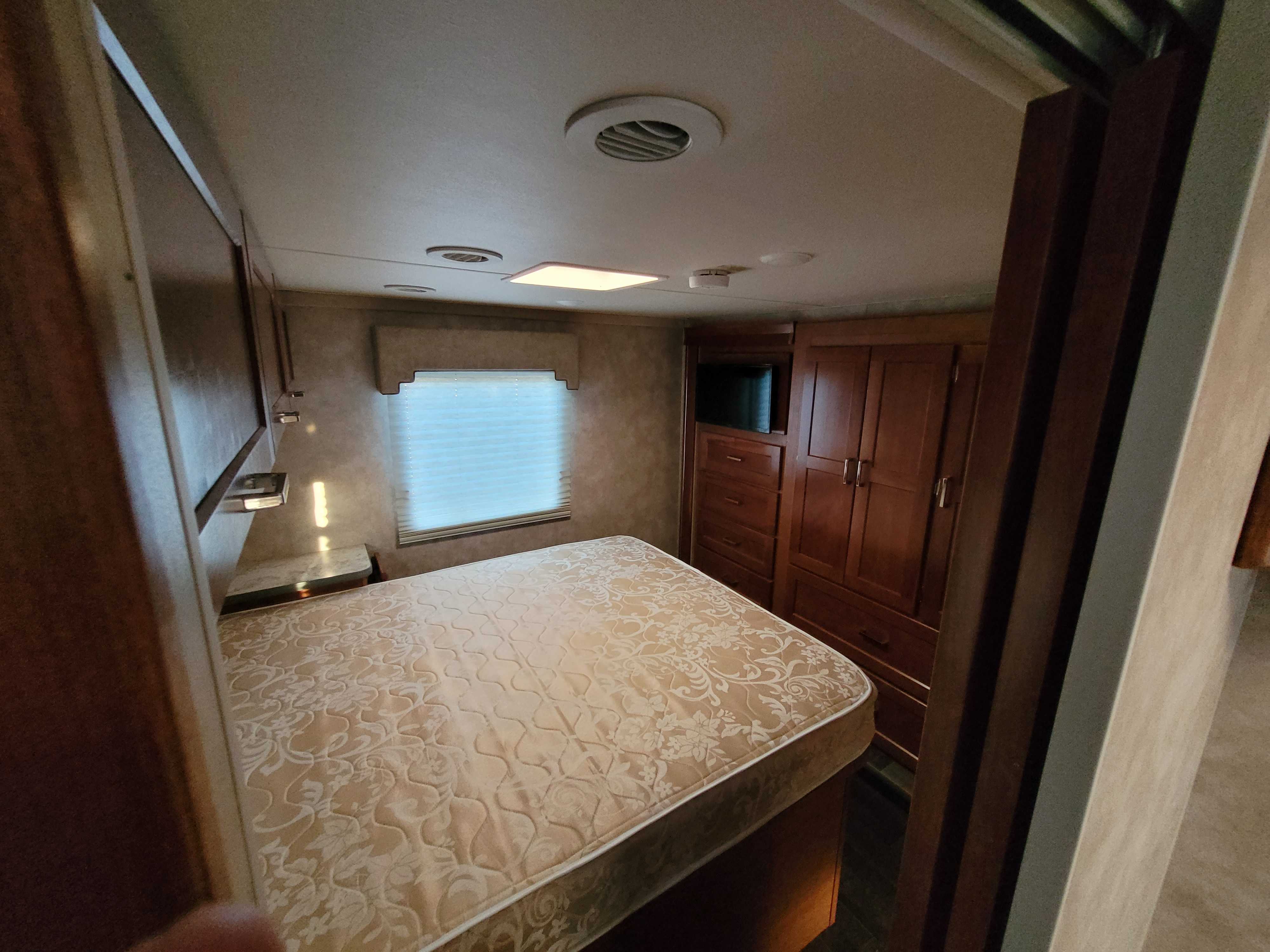Spacious RV rental bedroom with a patterned mattress, window, built-in storage, and TV, offering comfortable travel.. Winnebago Minnie Winnie 2018