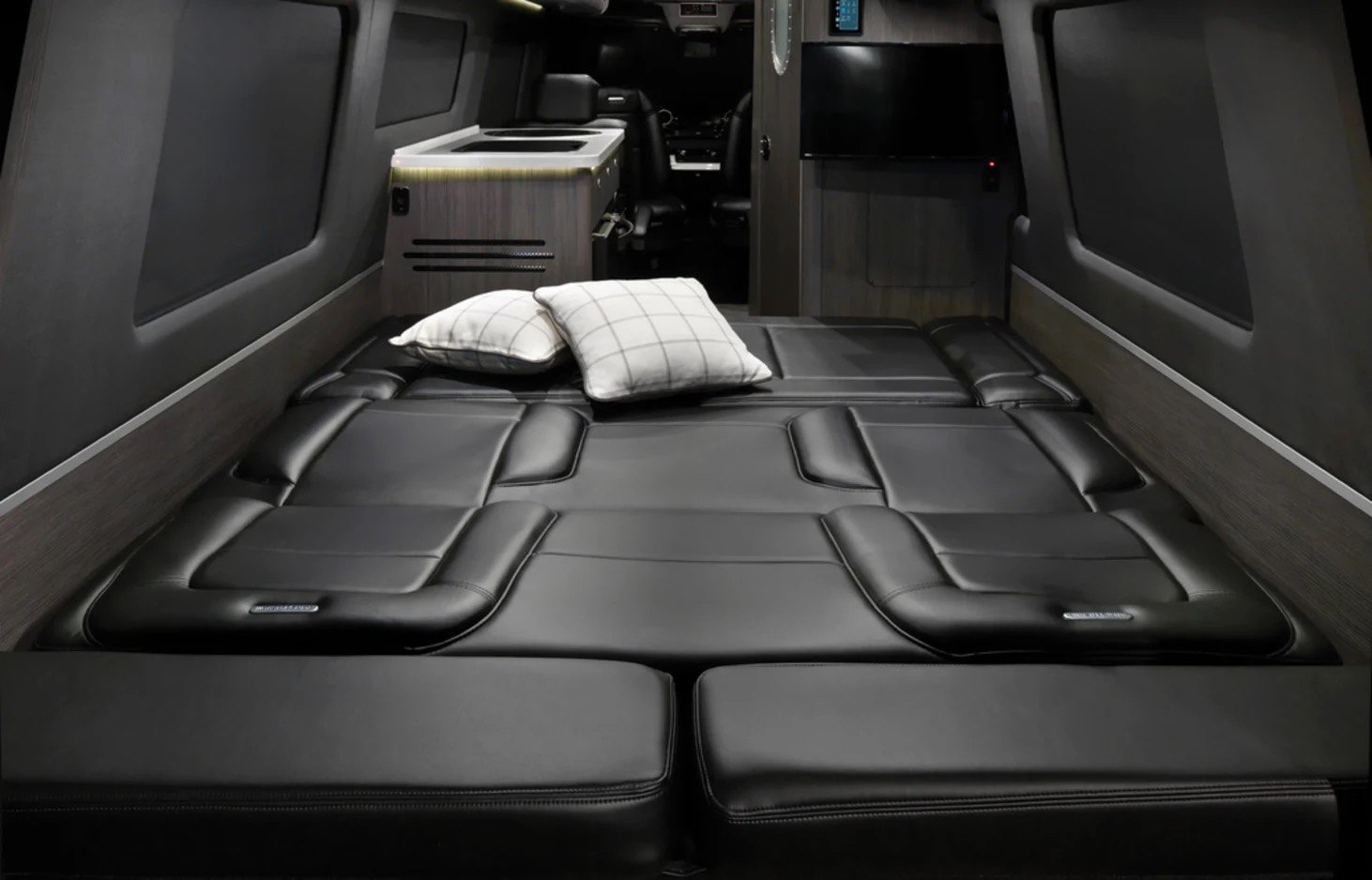 Comfortable black leather bed in an RV rental. Modern camper van interior with kitchenette and TV.. Airstream Interstate 2021