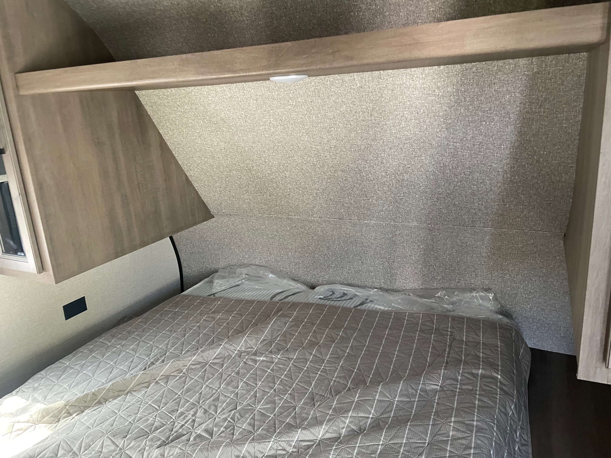 Compact RV rental bedroom showcasing a quilted bed, textured walls, overhead storage, and plastic-wrapped items.. Starcraft Autumn Ridge 2022