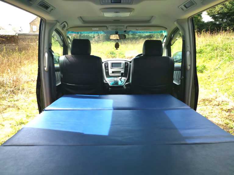 This RV rental shows a minivan interior with a blue, flat sleeping platform stretching to the front seats, ready for camping.. Toyota Other 2022