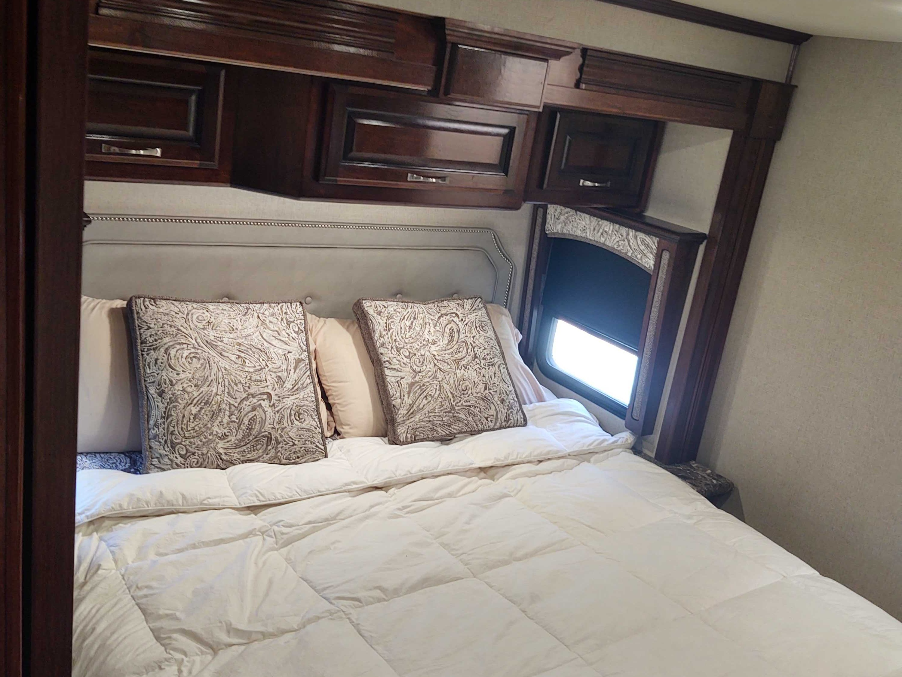 Experience comfort in this cozy RV rental bedroom. Features a soft bed, upholstered headboard, overhead cabinets, and window.. Fleetwood Pace Arrow 2018