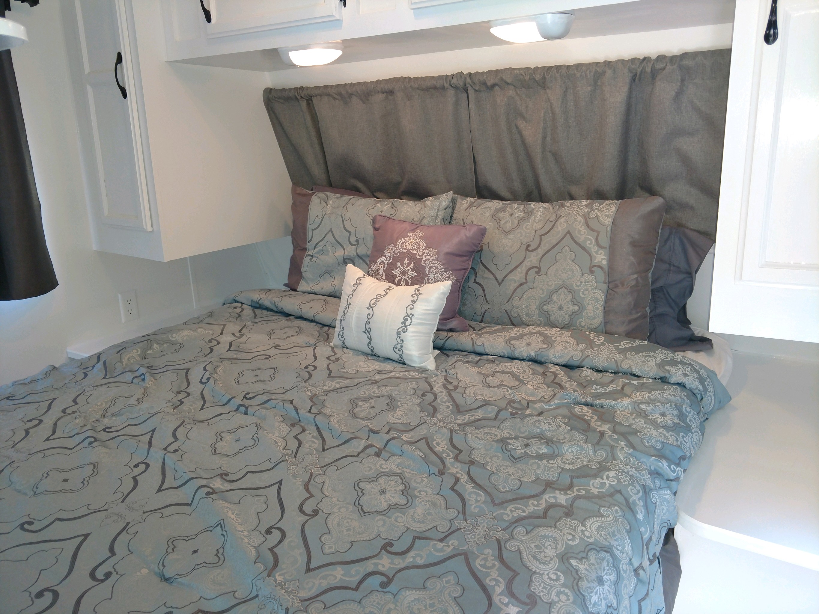 Cozy RV rental bedroom with light blue & grey patterned bedding, lavender pillows, and white overhead cabinets.. Jayco Jay Flight 2006